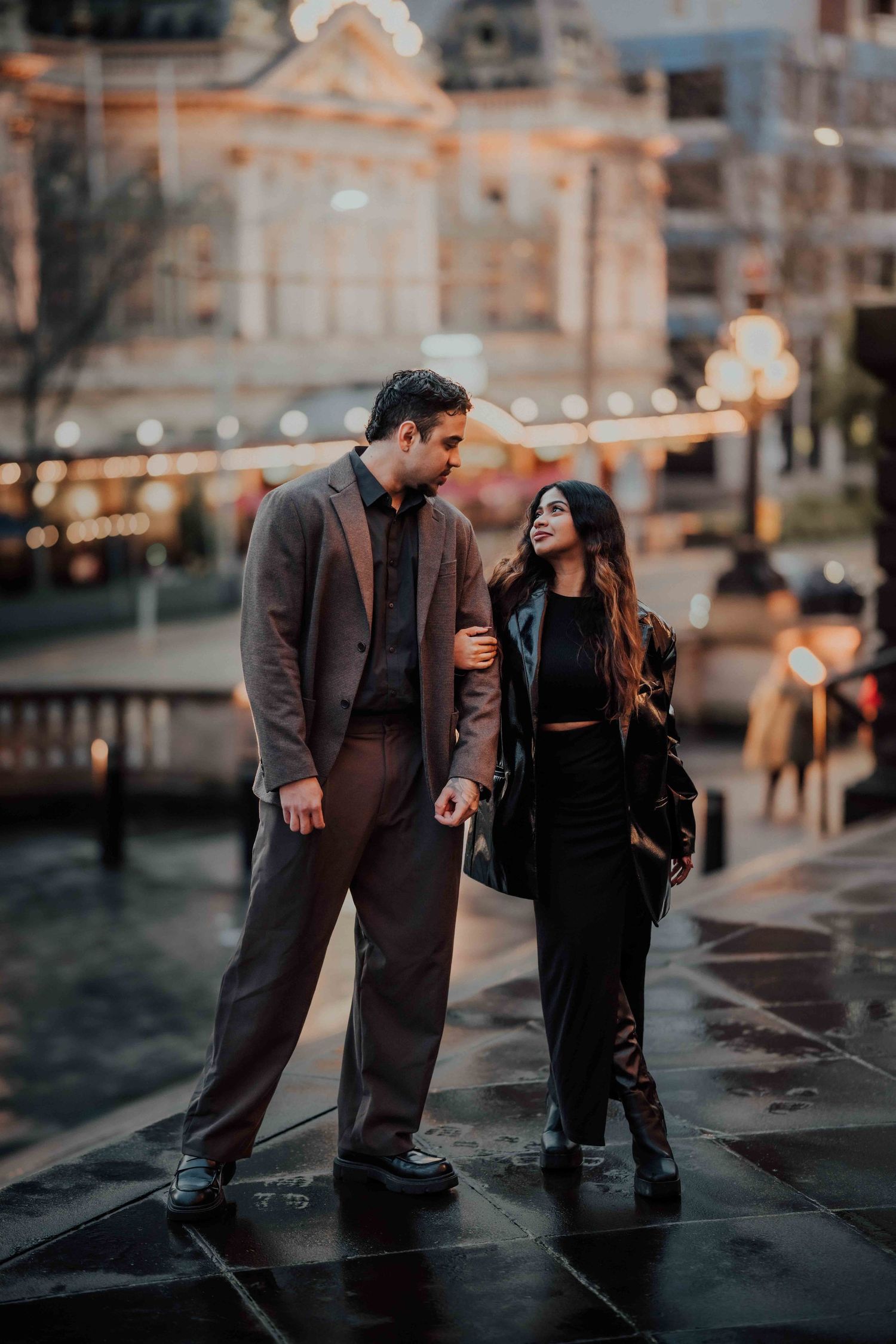 Elegant couple walking together on a rain-soaked city street with bokeh lights.