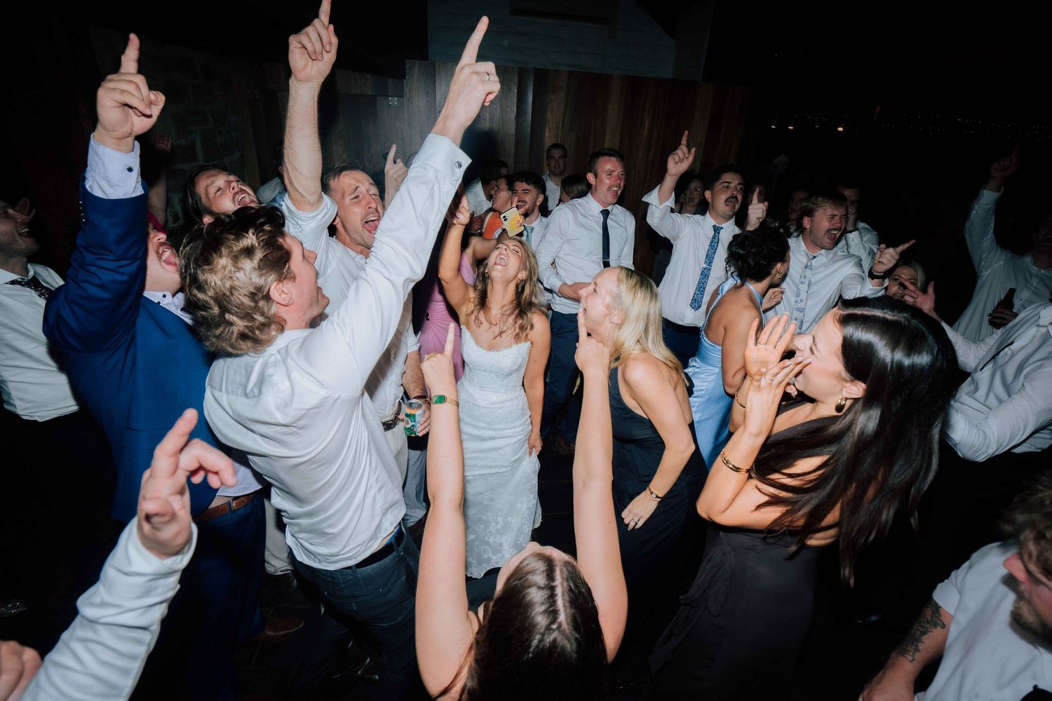 Bride and groom celebrate with guests on a lively wedding reception dance floor.