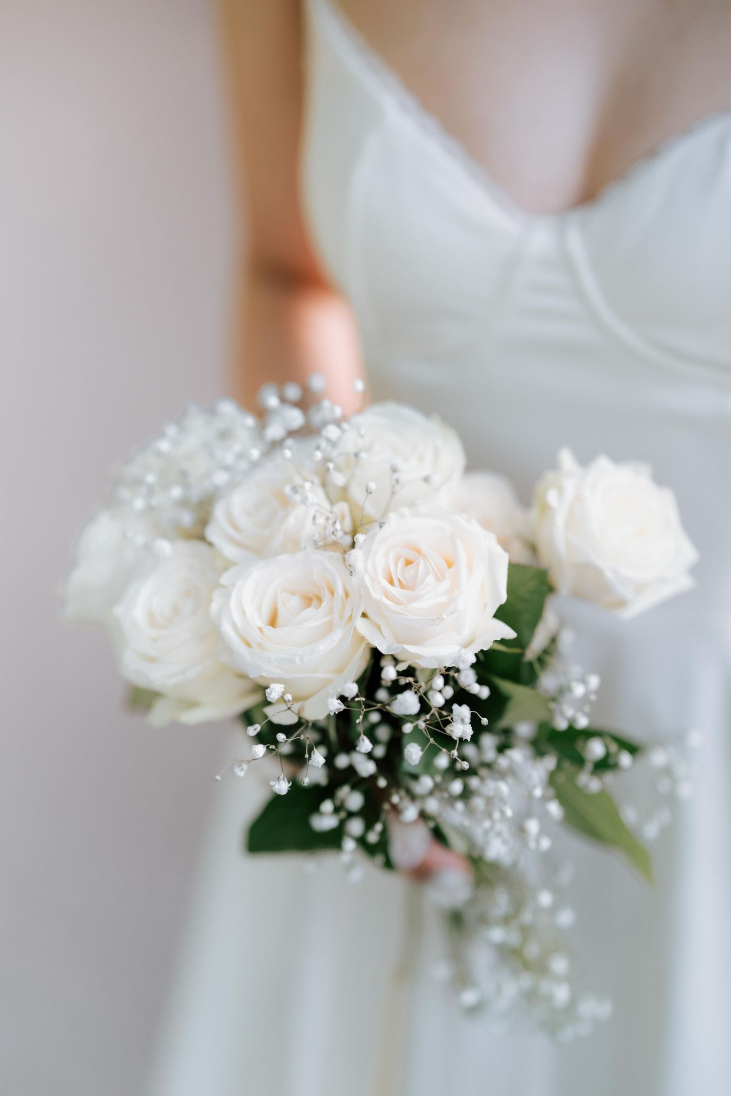 Bride holding a delicate bouquet of white roses and baby's breath in a white wedding dress.