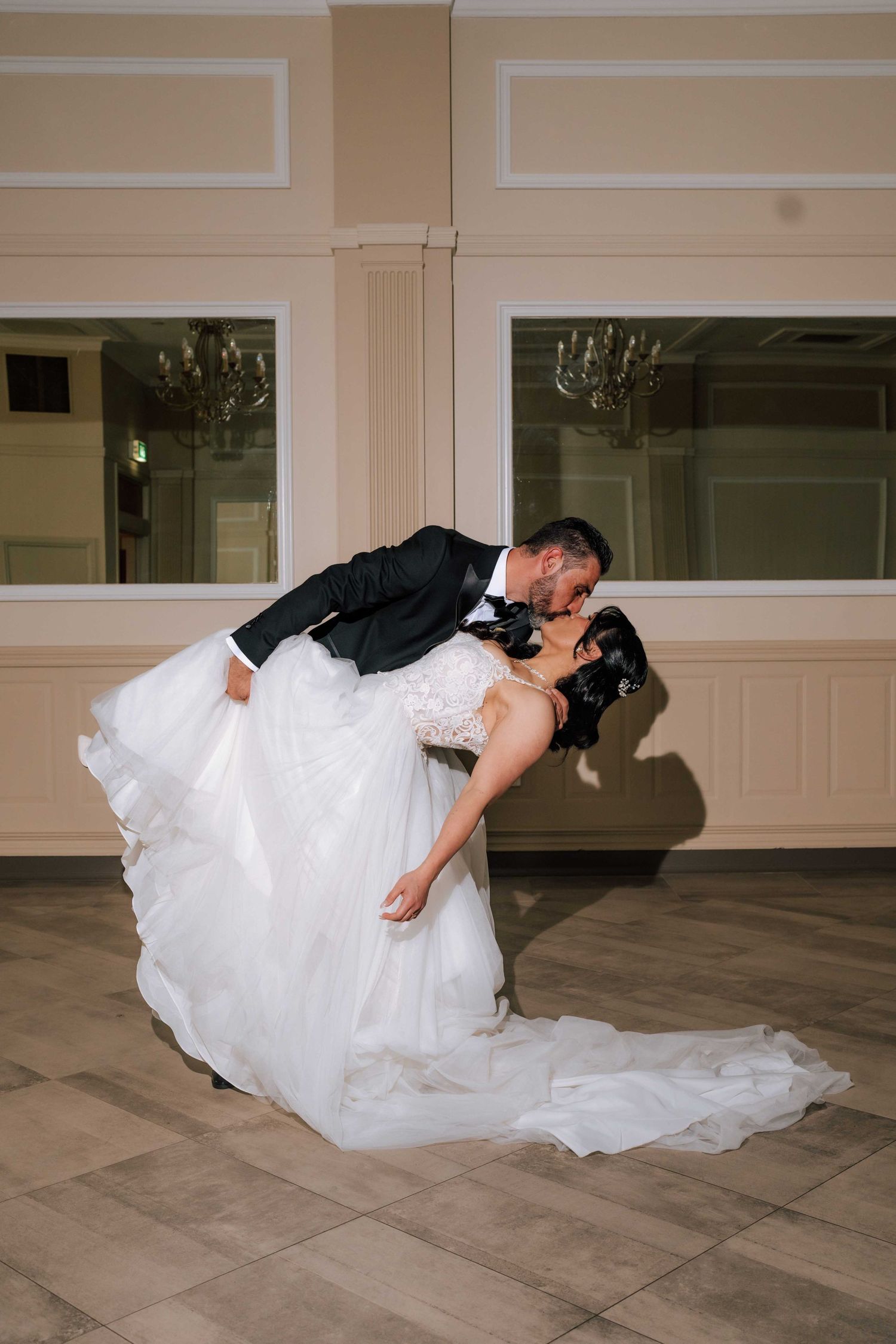 Groom dips bride for romantic kiss on dance floor during elegant wedding reception.