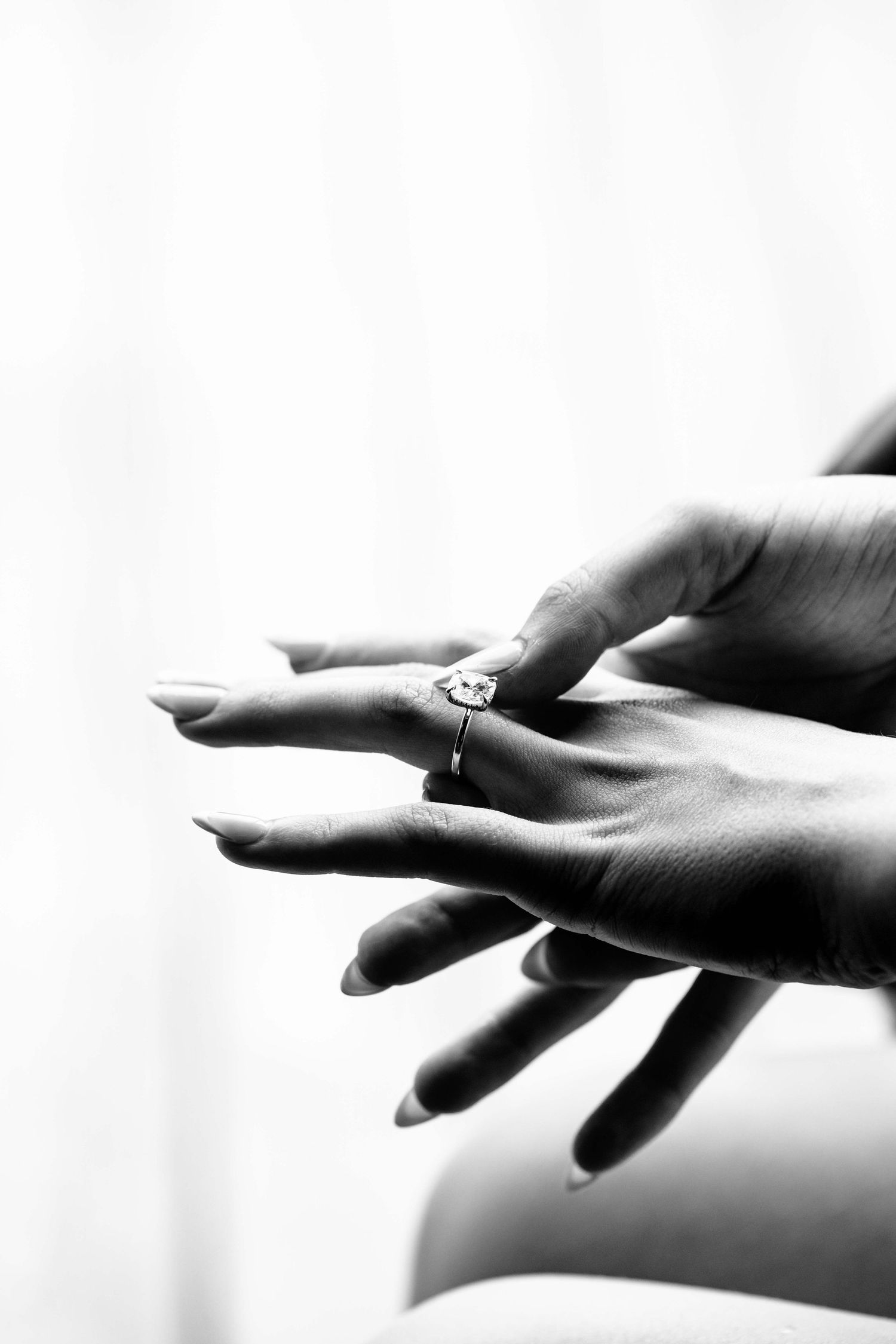 Black and white close-up of bride's hands showcasing elegant diamond engagement ring.