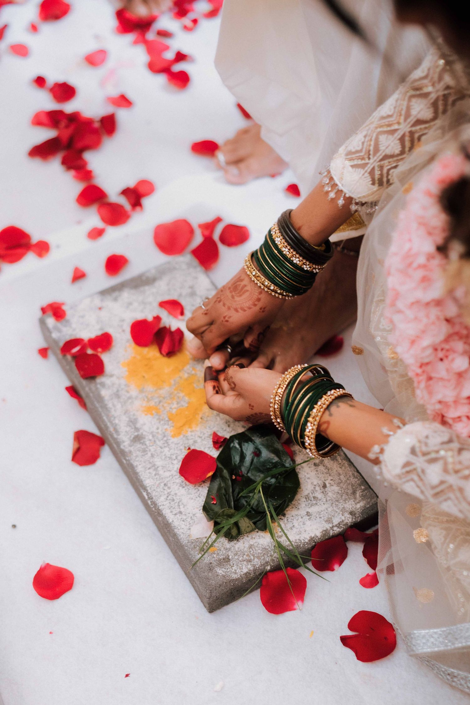 Close-up of bride's henna-adorned hands with green gold bangles performing Hindu wedding ritual.