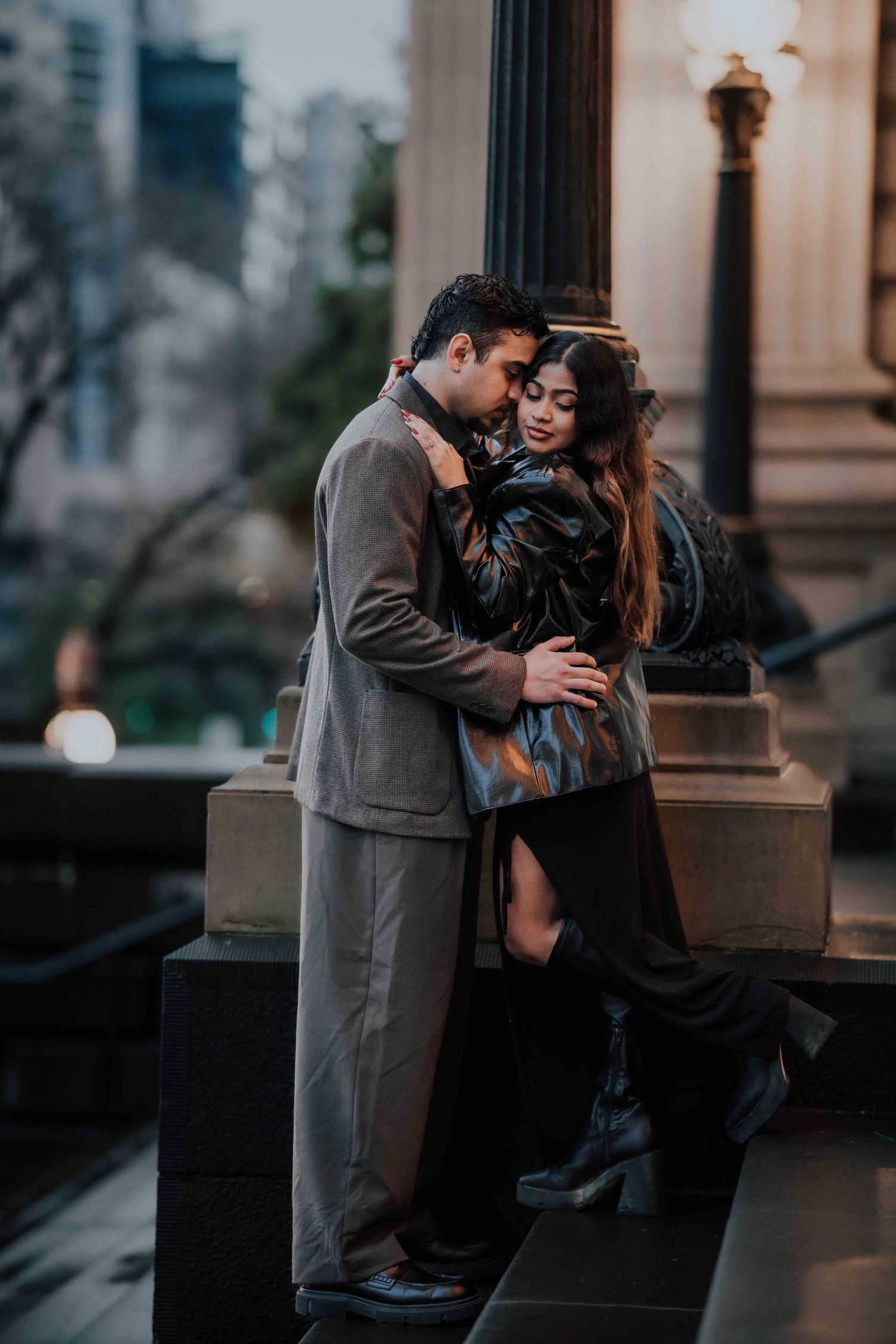 Couple sharing an intimate embrace beside an ornate lamppost in a city at dusk.