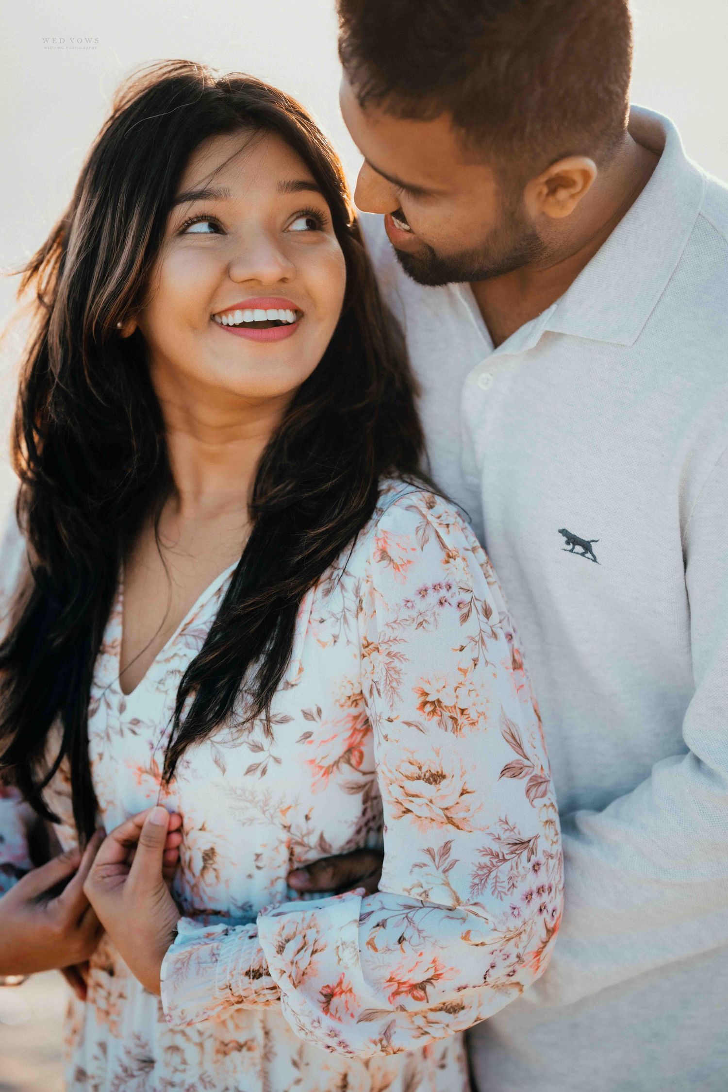 Couple sharing a tender moment outdoors, woman in floral dress laughing joyfully as partner leans close.