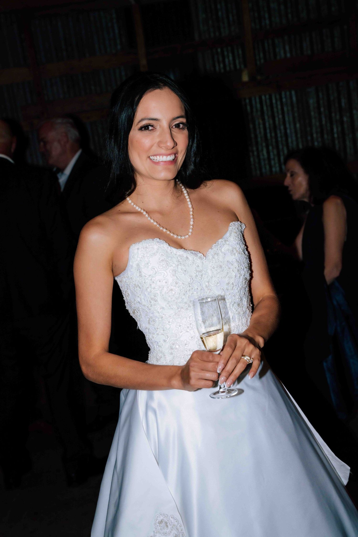 Beautiful bride in white strapless gown holding champagne glass with pearl necklace.