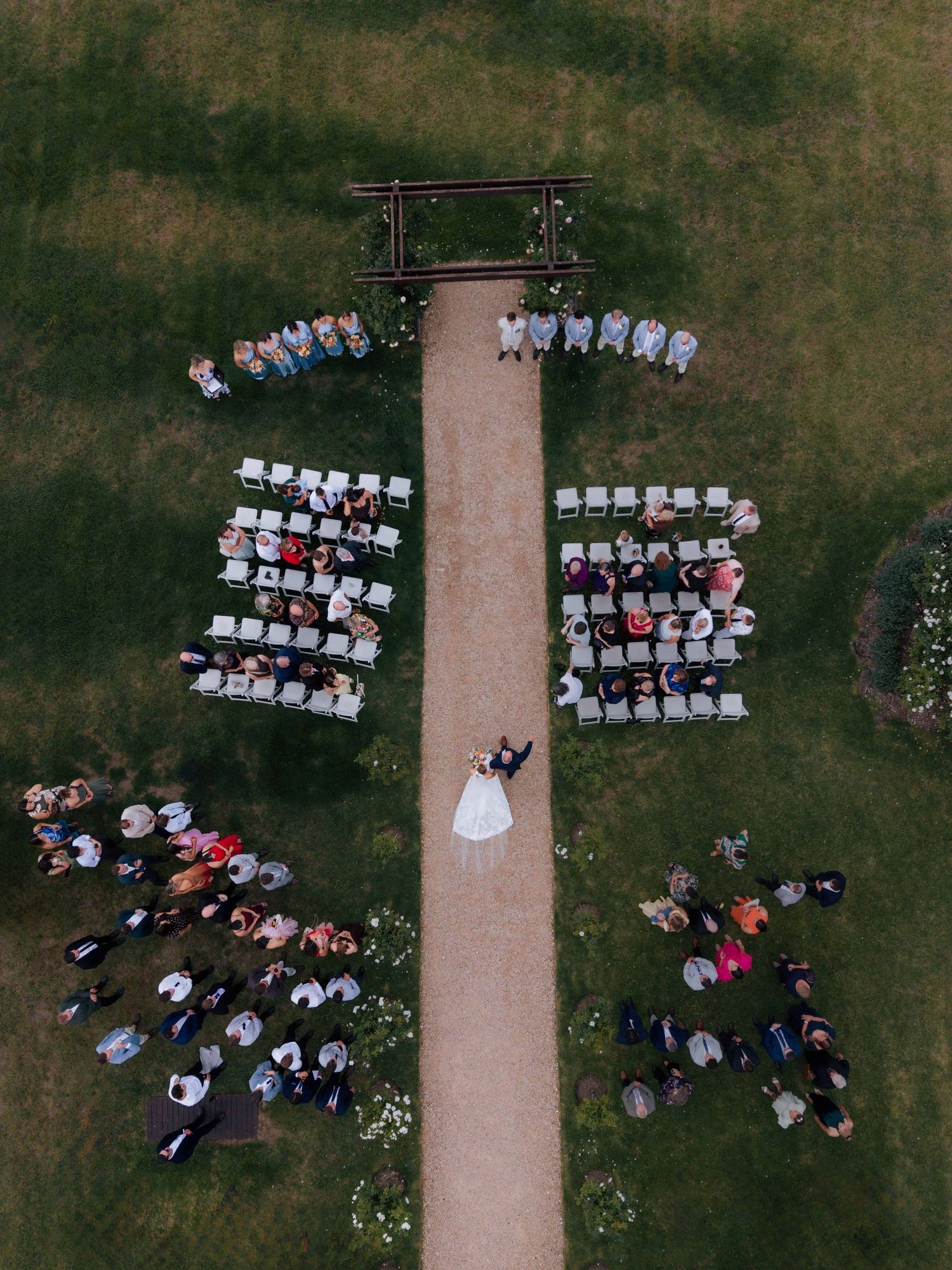 Aerial drone view of outdoor wedding ceremony with guests seated on either side of aisle.