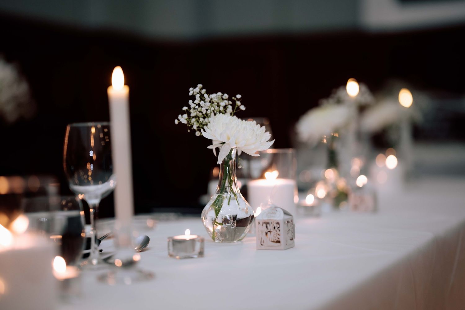 Close-up of wedding reception table with white chrysanthemum, taper candle, and tea lights.
