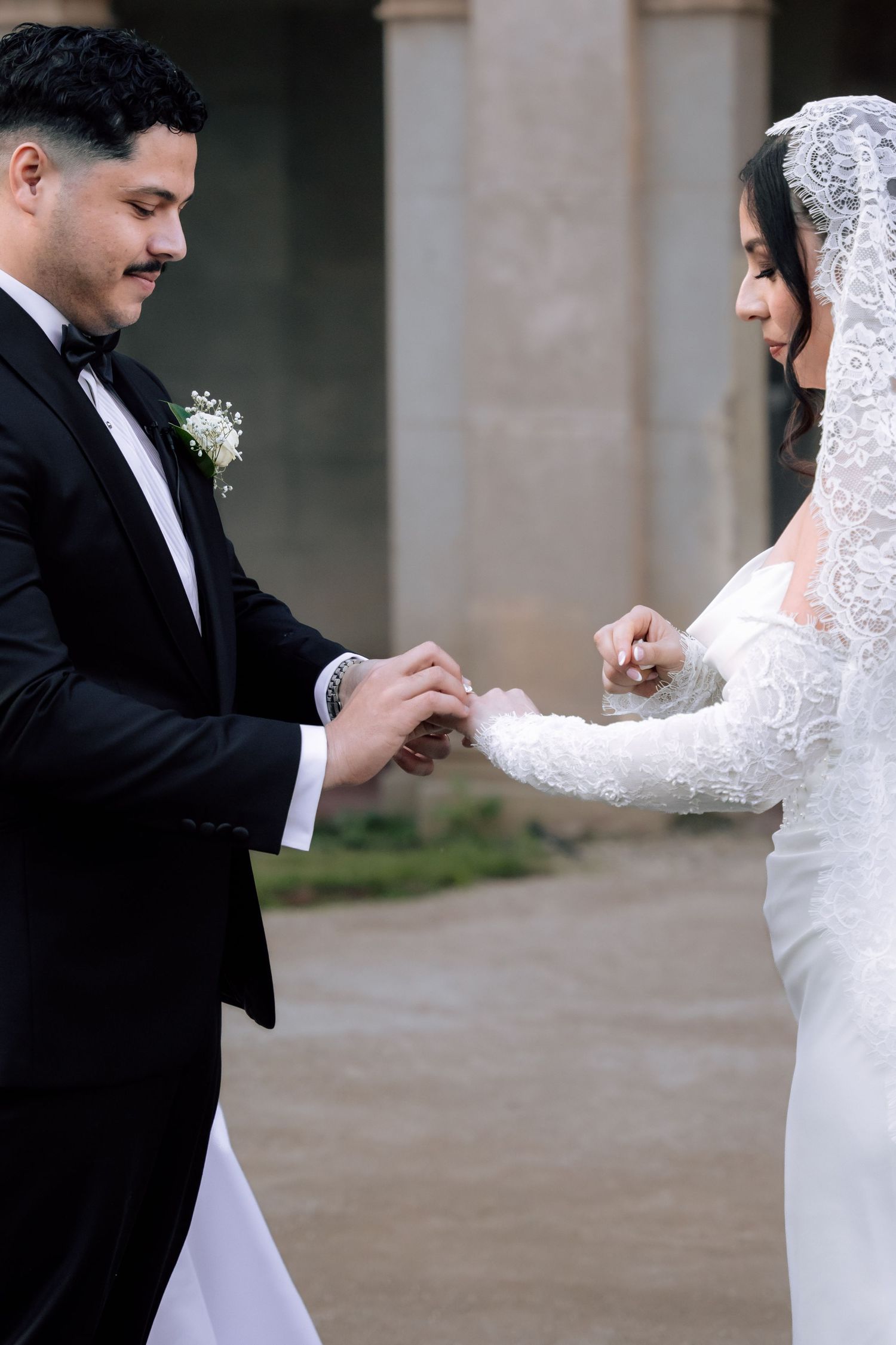 Bride and groom exchange rings during outdoor wedding ceremony beside stone columns.