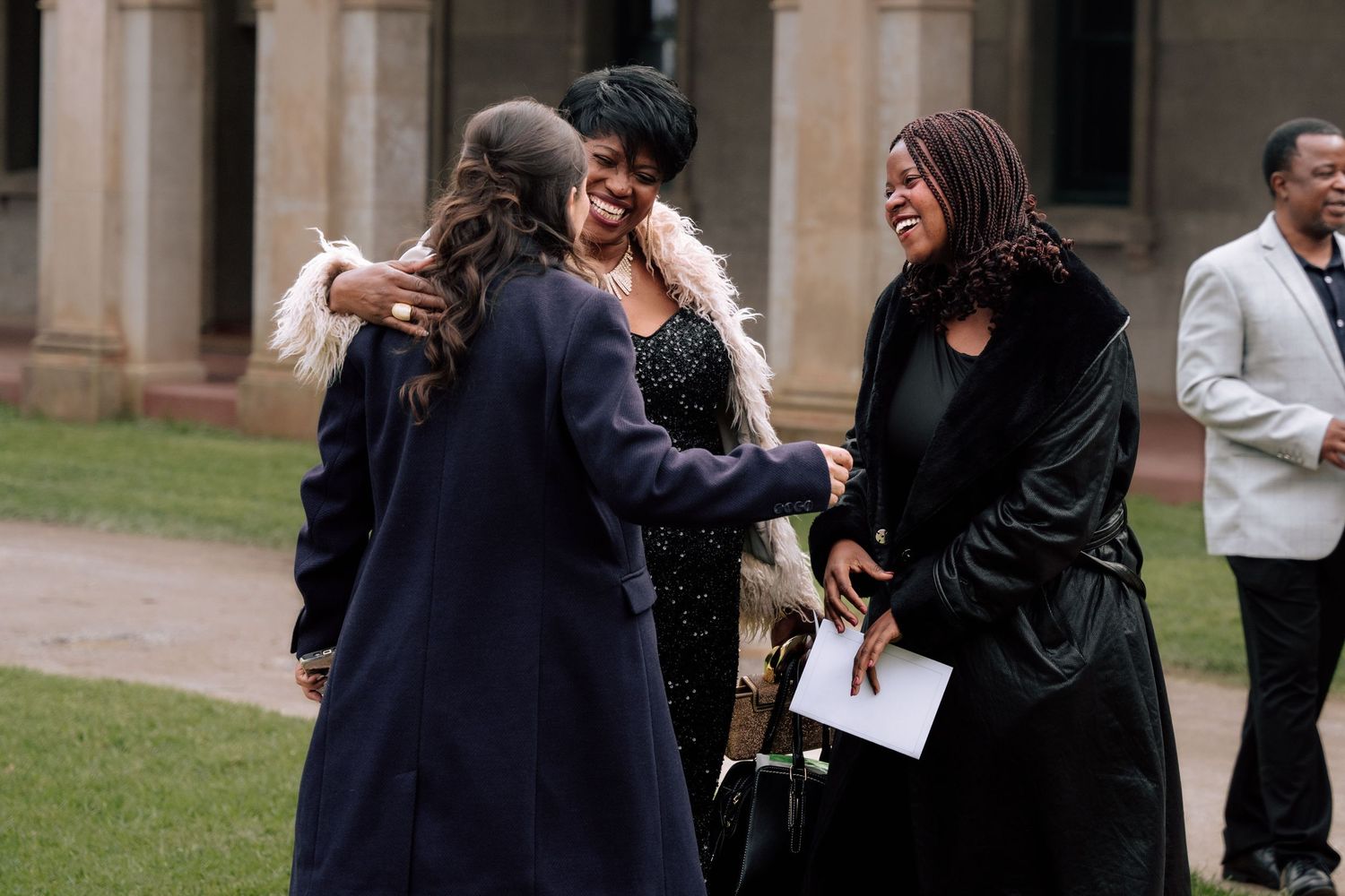 Wedding guests sharing warm embraces and laughter outside historic stone building.