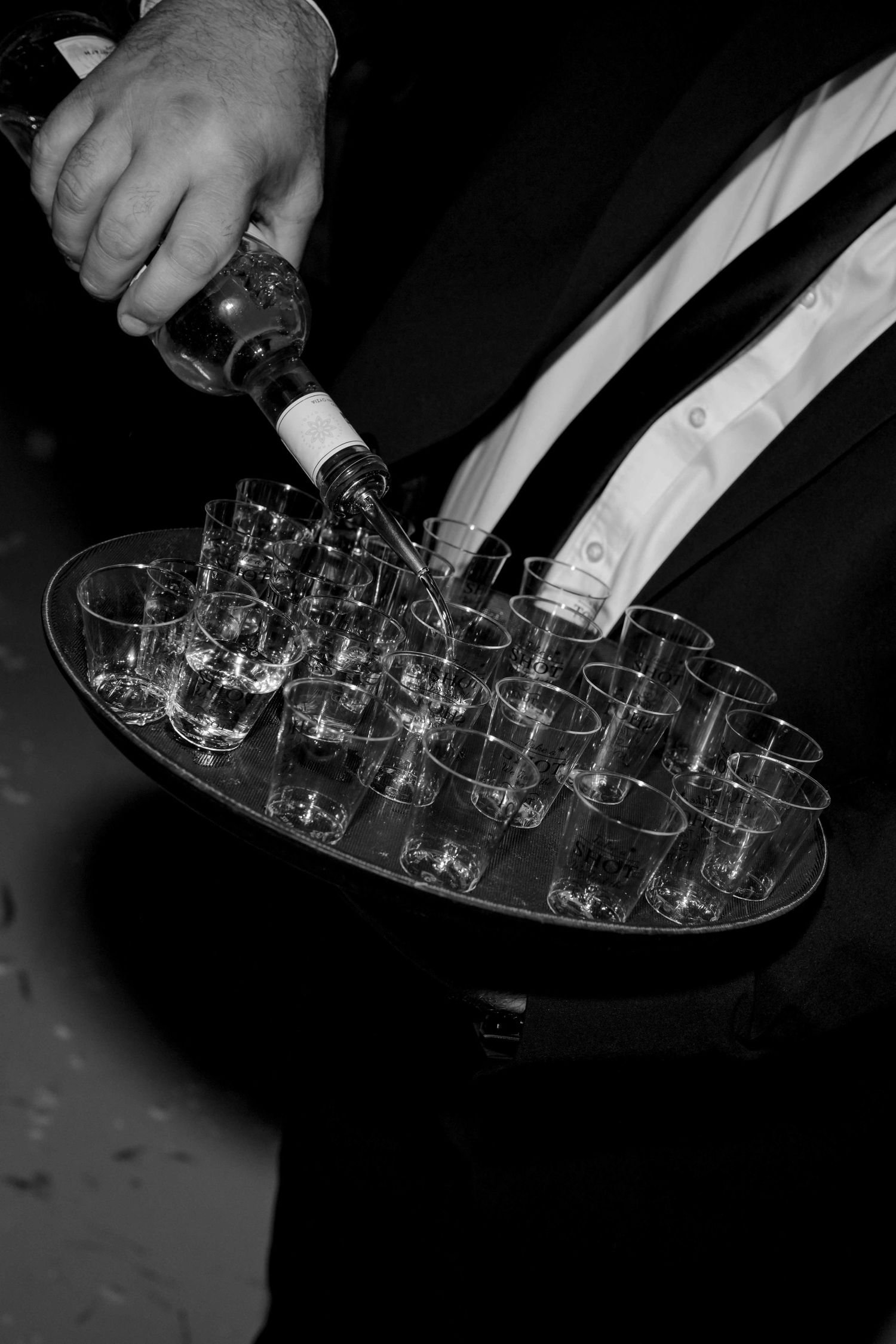 Wedding waiter pouring drinks into shot glasses on tray at reception.