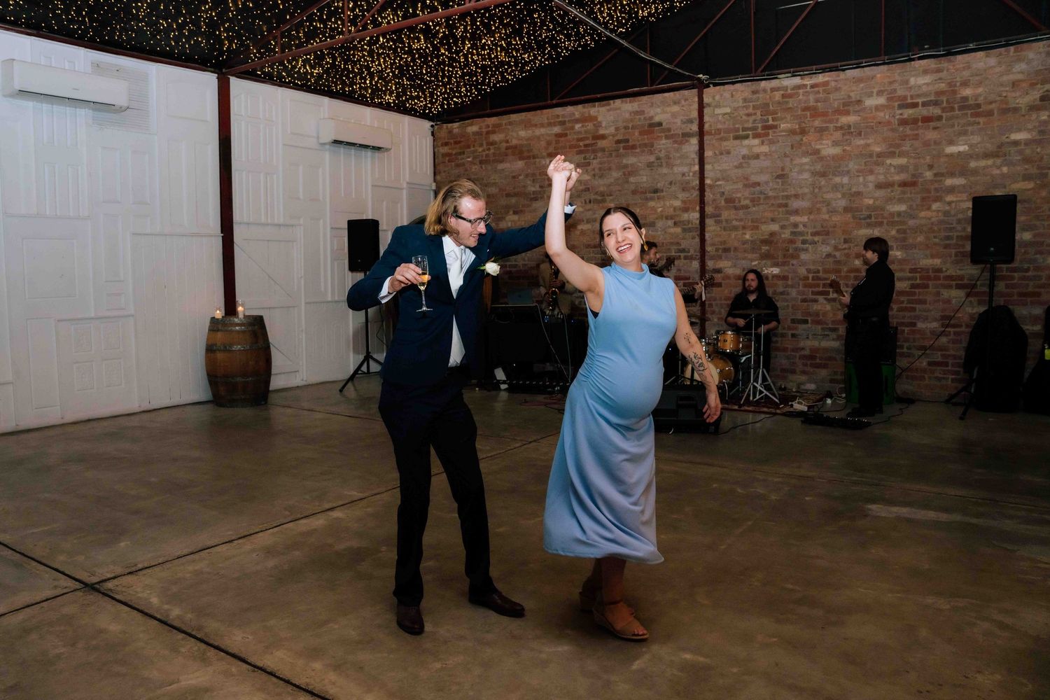 Couple dancing joyfully on wedding reception dance floor in rustic venue.