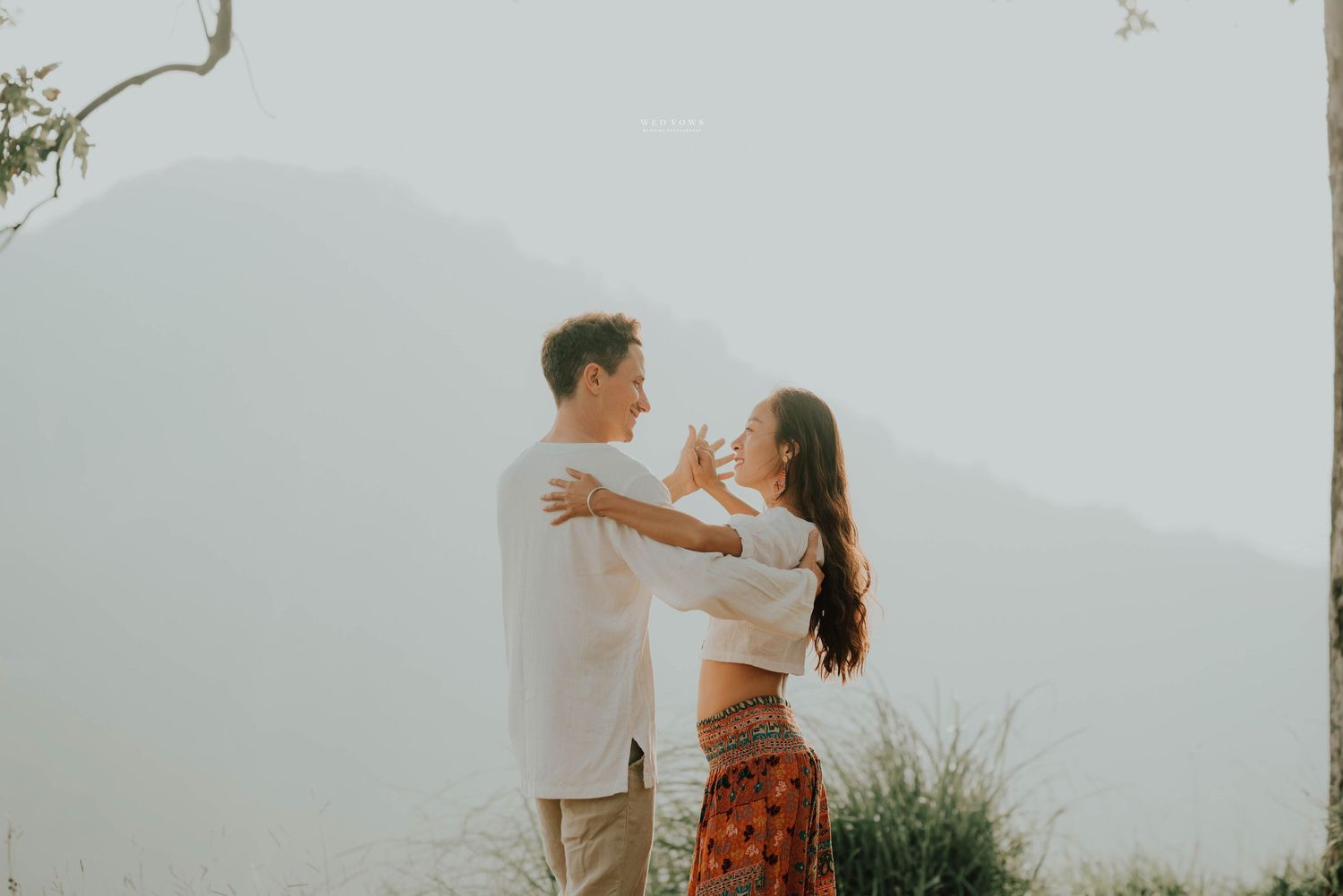 Happy couple dancing together on a hilltop with misty mountains in background.