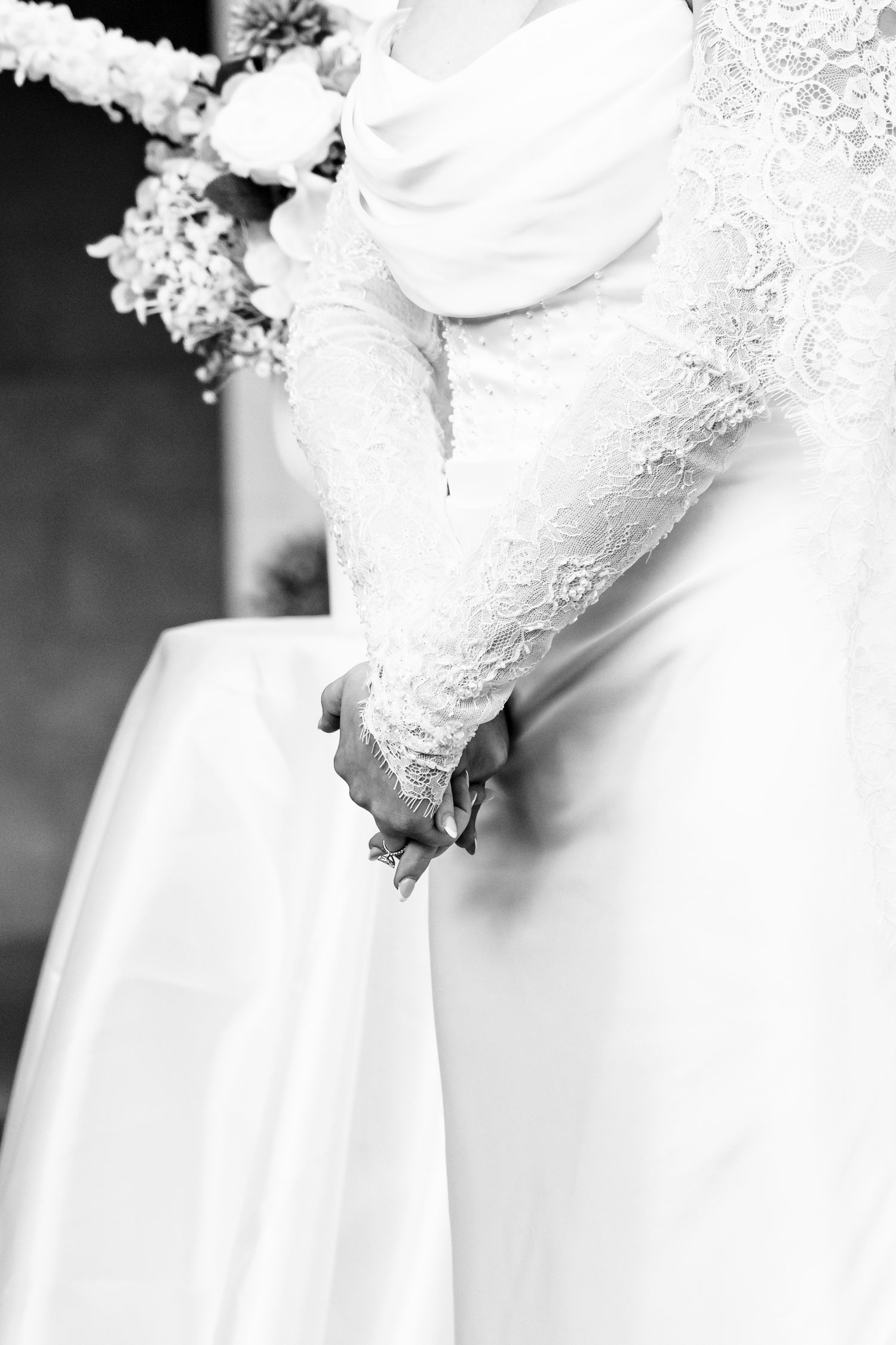 Close-up black and white photo of a bride in a lace long-sleeve wedding gown holding her bouquet.