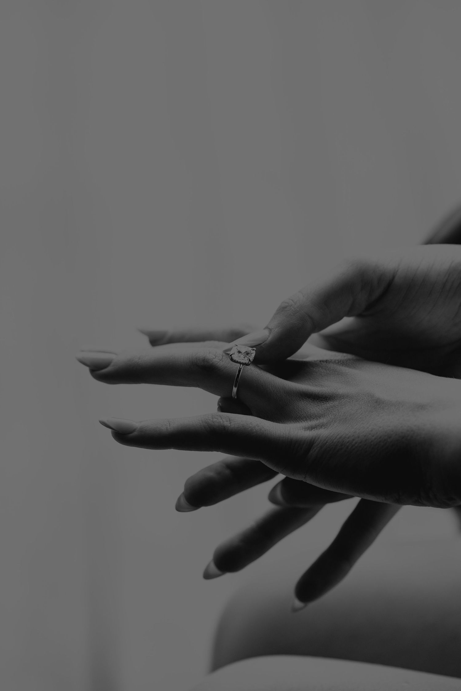 Black and white photo of hands placing a diamond engagement ring on a finger.