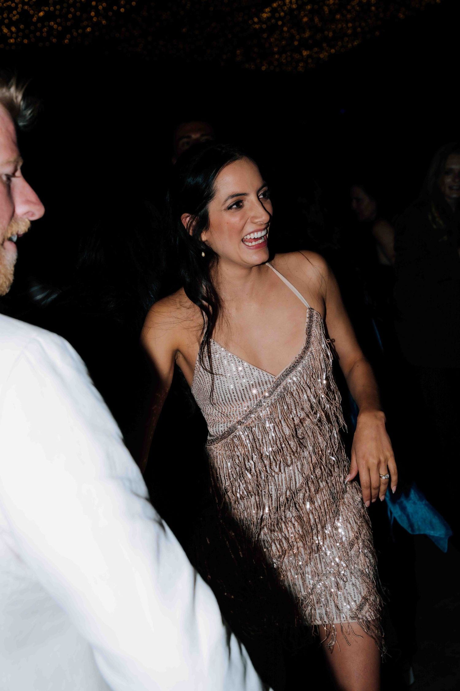 Bride laughing joyfully in a sparkling silver fringe dress during wedding reception dancing.
