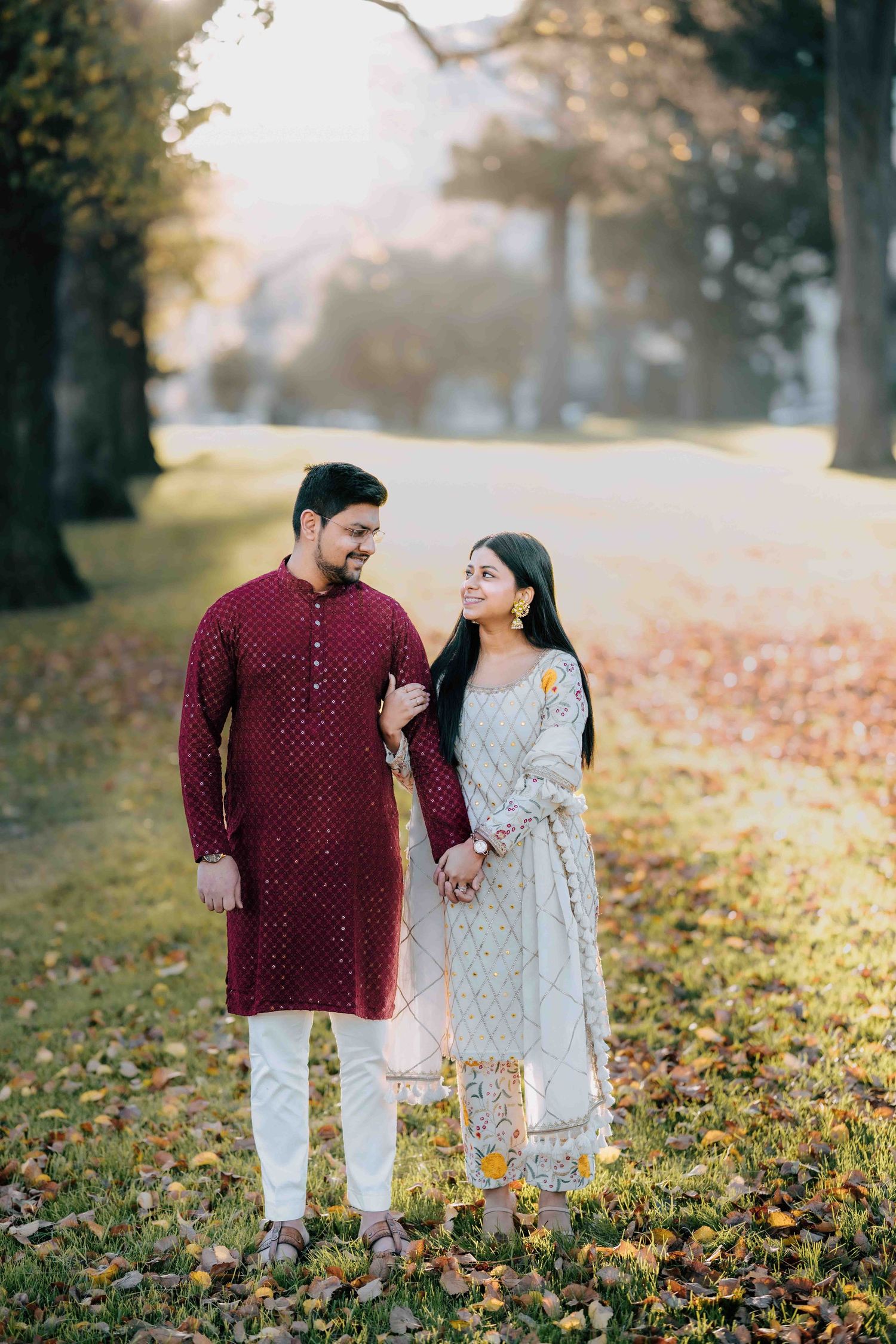 Indian couple holding hands in a sunlit autumn park wearing traditional kurta and salwar.