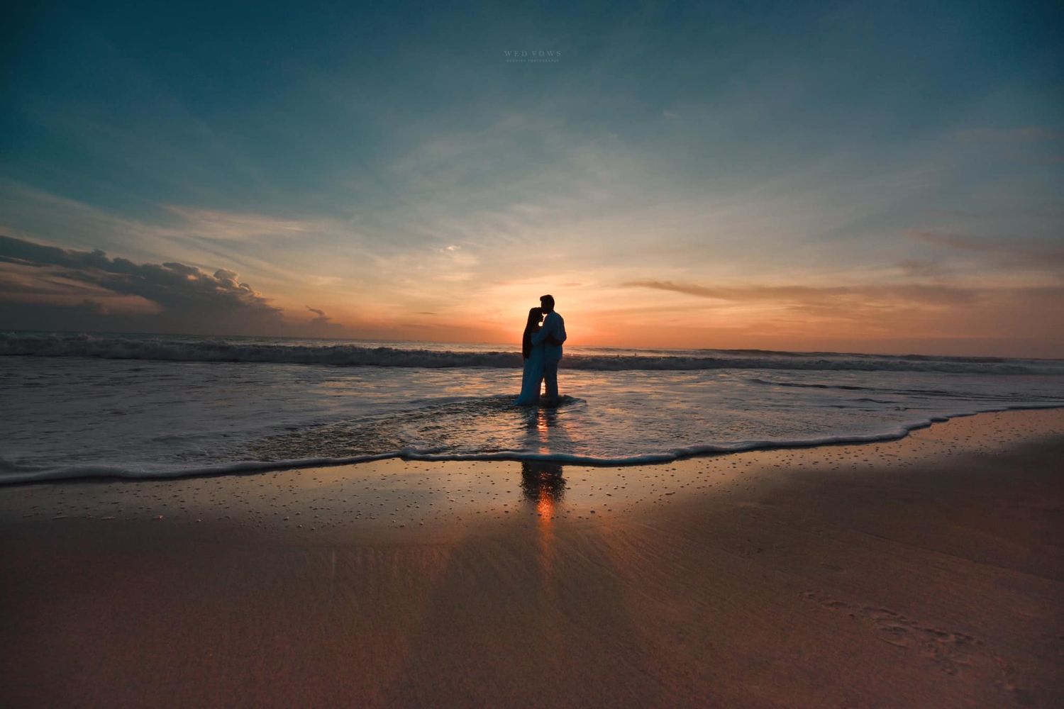 Romantic couple silhouetted against a stunning sunset on a calm beach.