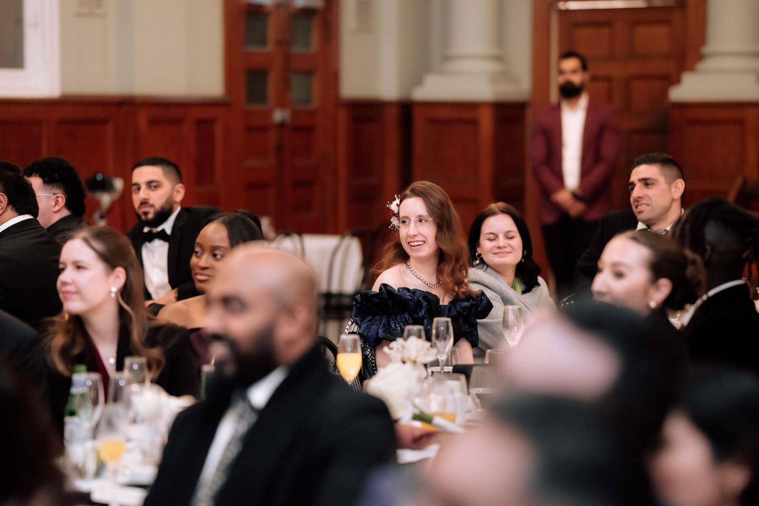 Elegantly dressed guests seated at tables during a formal gala dinner in a grand banquet hall.