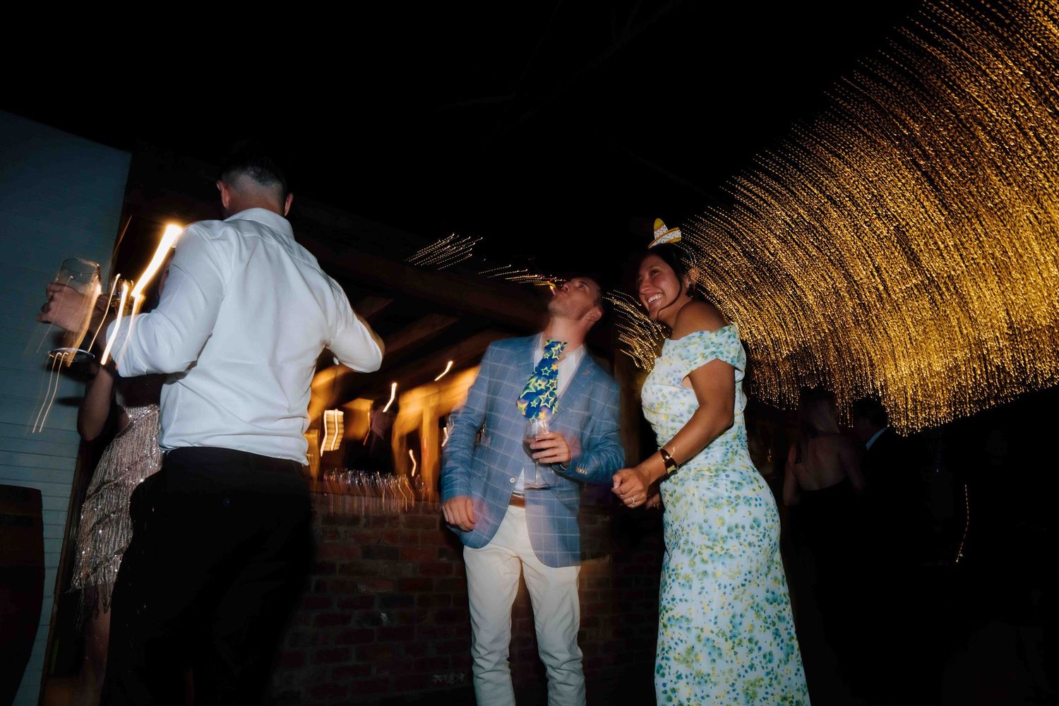 Couple dancing outdoors at night near thatched decor at a wedding reception celebration.