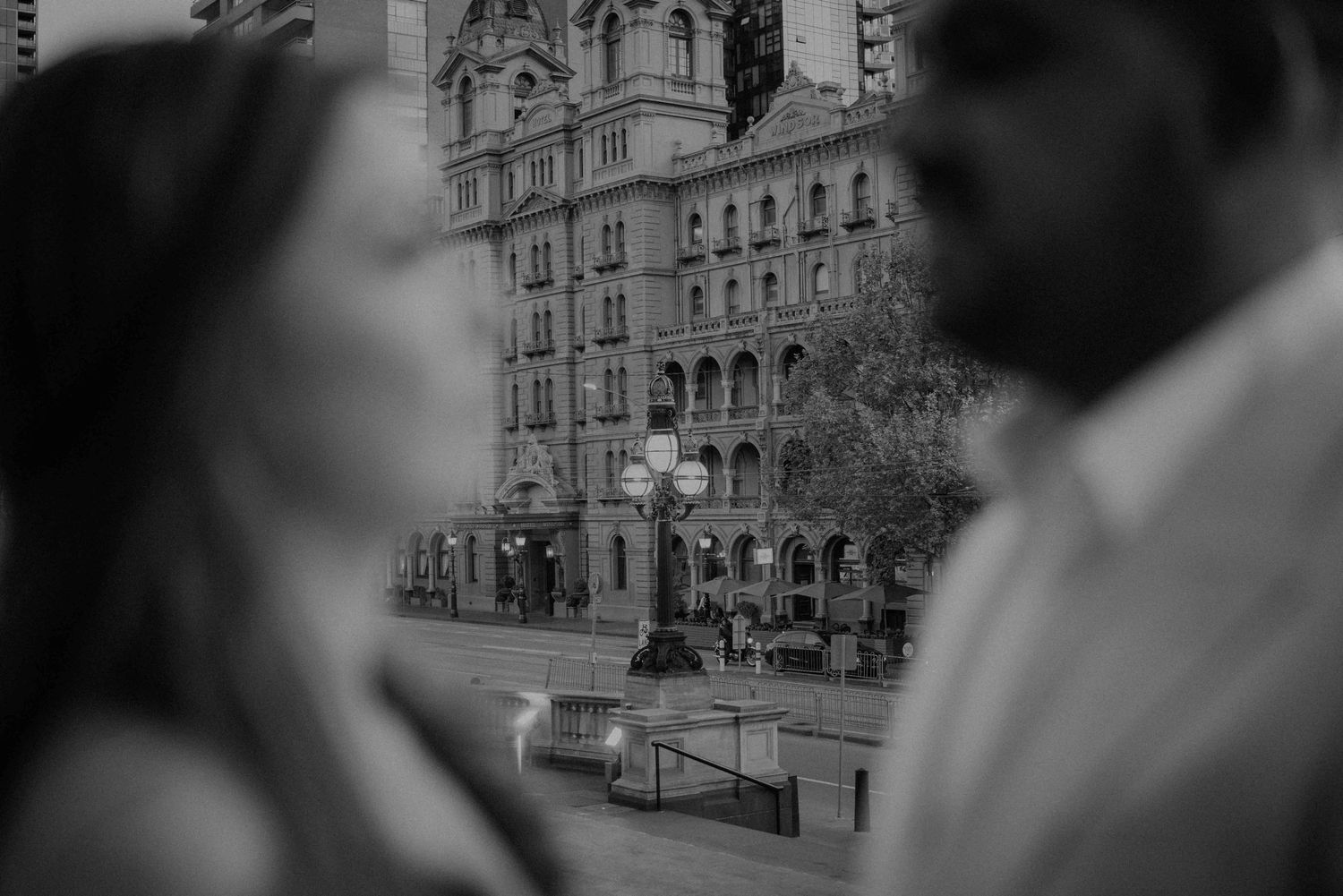 Black and white artistic wedding photo of a couple facing each other with a grand city building in background.