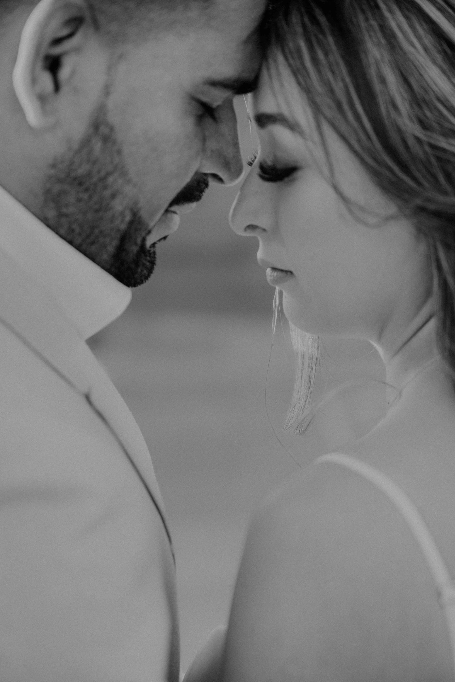 Intimate black and white close-up of a wedding couple touching foreheads tenderly.