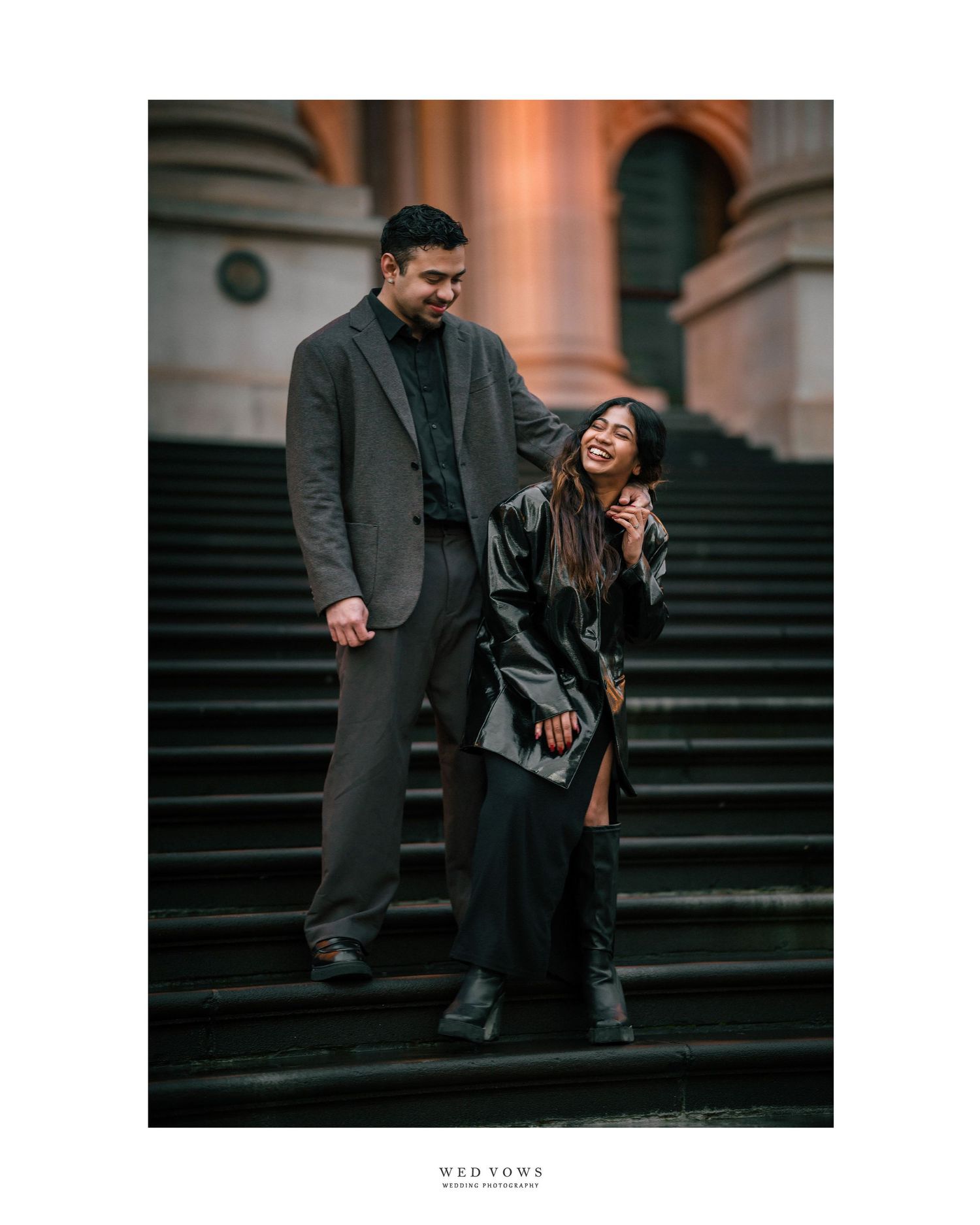 Couple laughing together on grand stone steps during an evening engagement photo session.