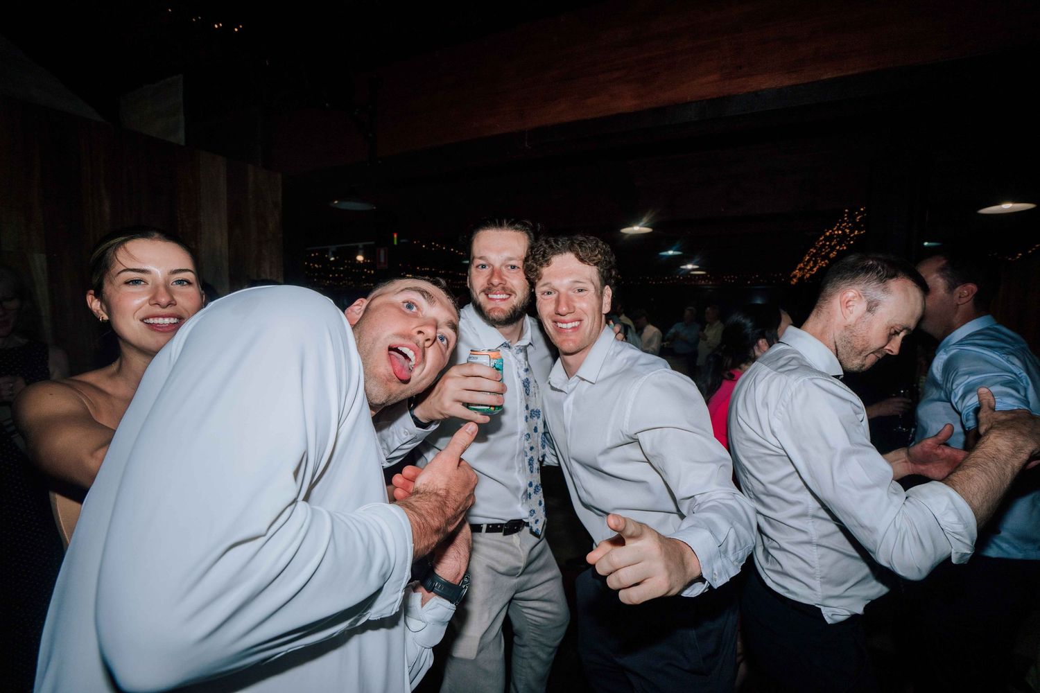 Group of groomsmen in white shirts laughing and dancing together at wedding reception party.