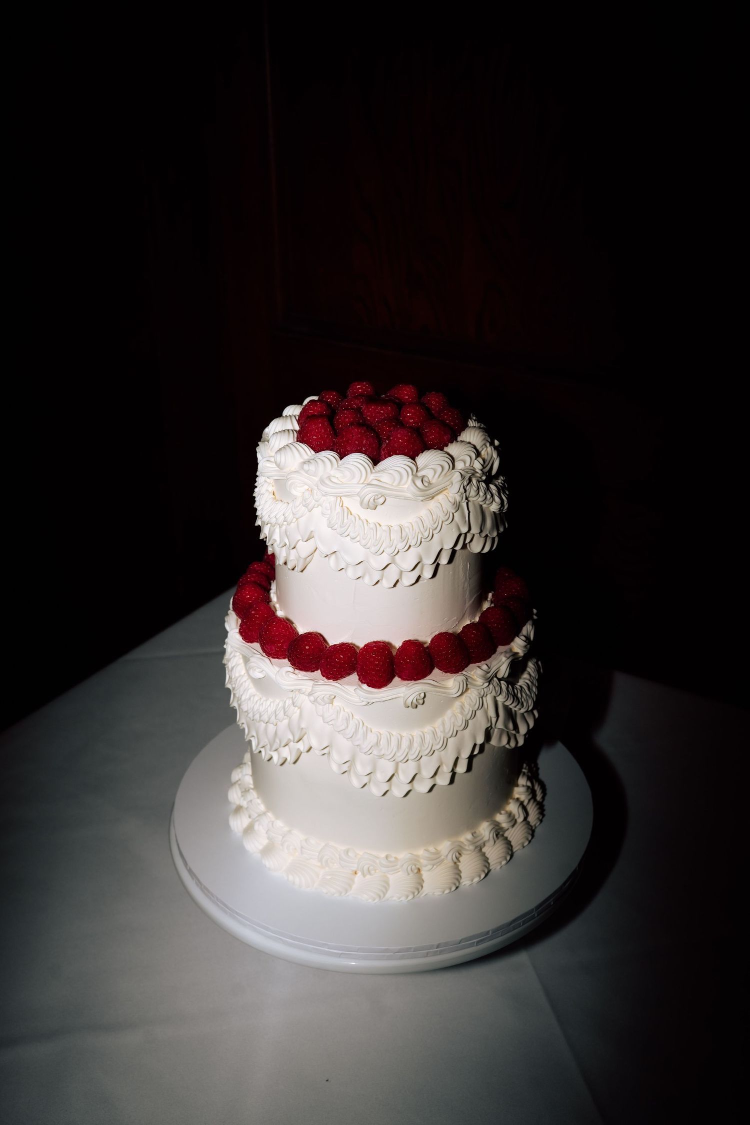 Two-tier white wedding cake decorated with red raspberries and intricate piped frosting details.