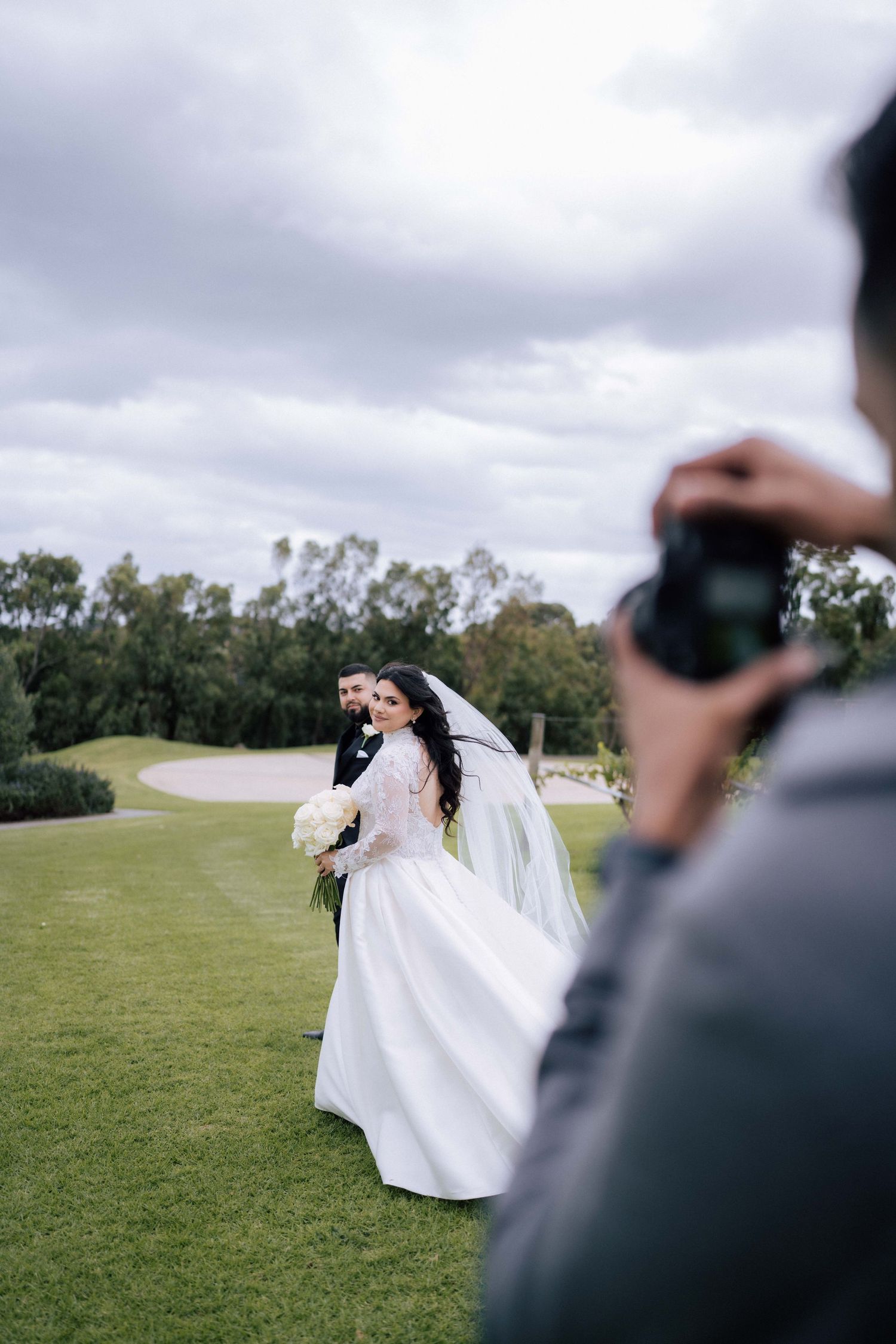 Wedding photographer captures bride and groom portrait session on lush green golf course under cloudy sky.