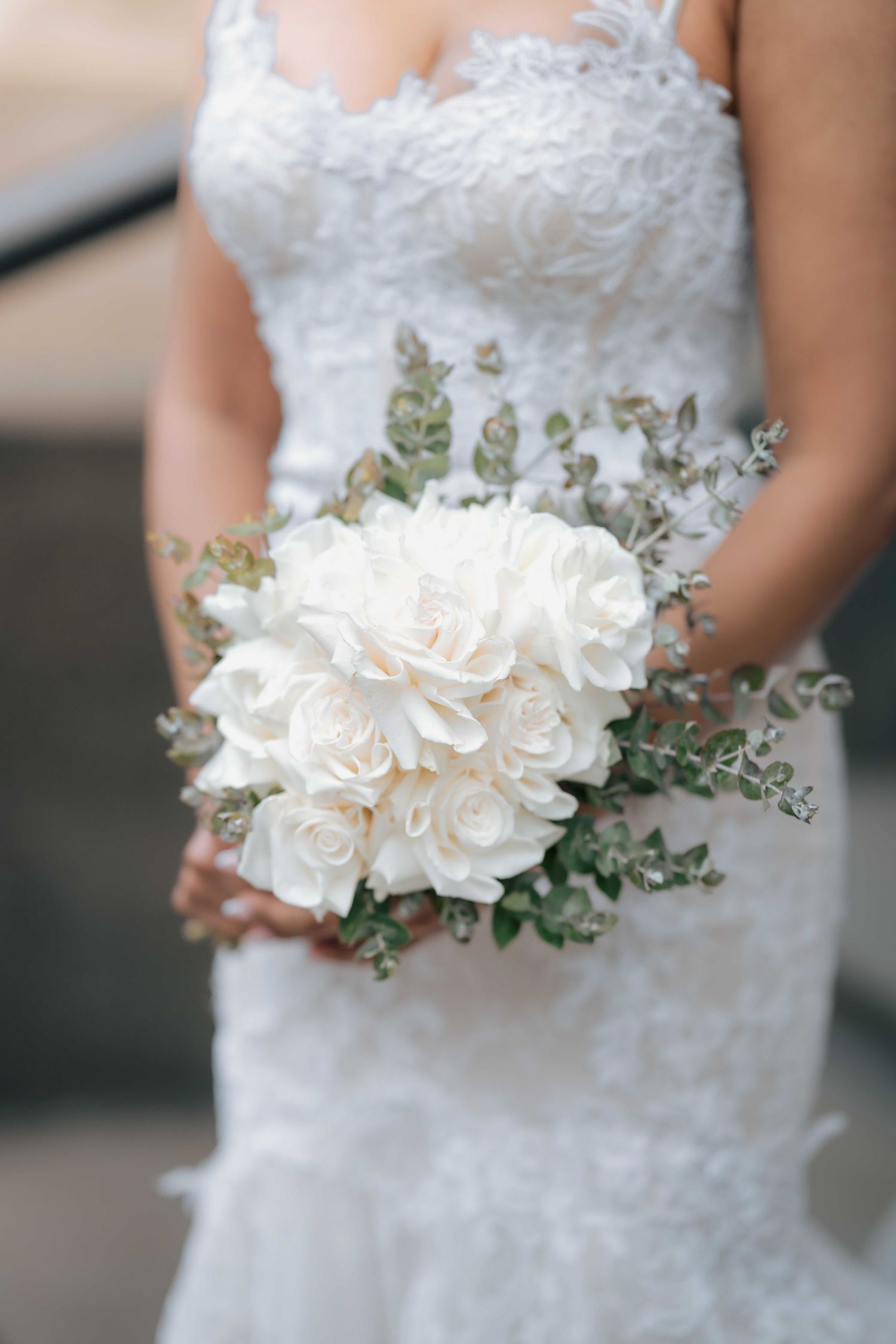 Bride holding elegant white rose and peony wedding bouquet with eucalyptus greenery accents.