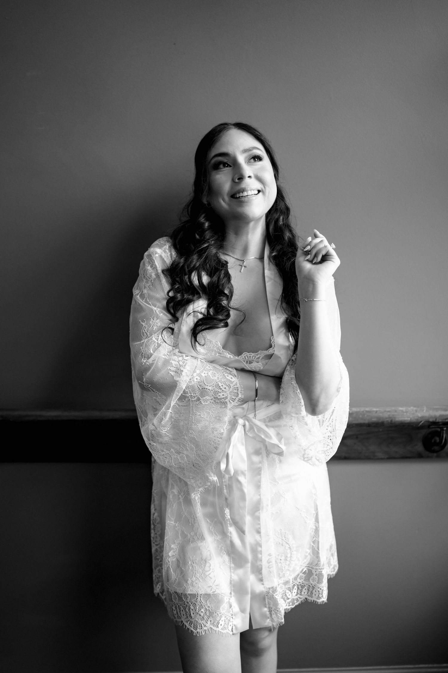 Black and white portrait of a smiling bride in a lace robe during wedding morning preparations.