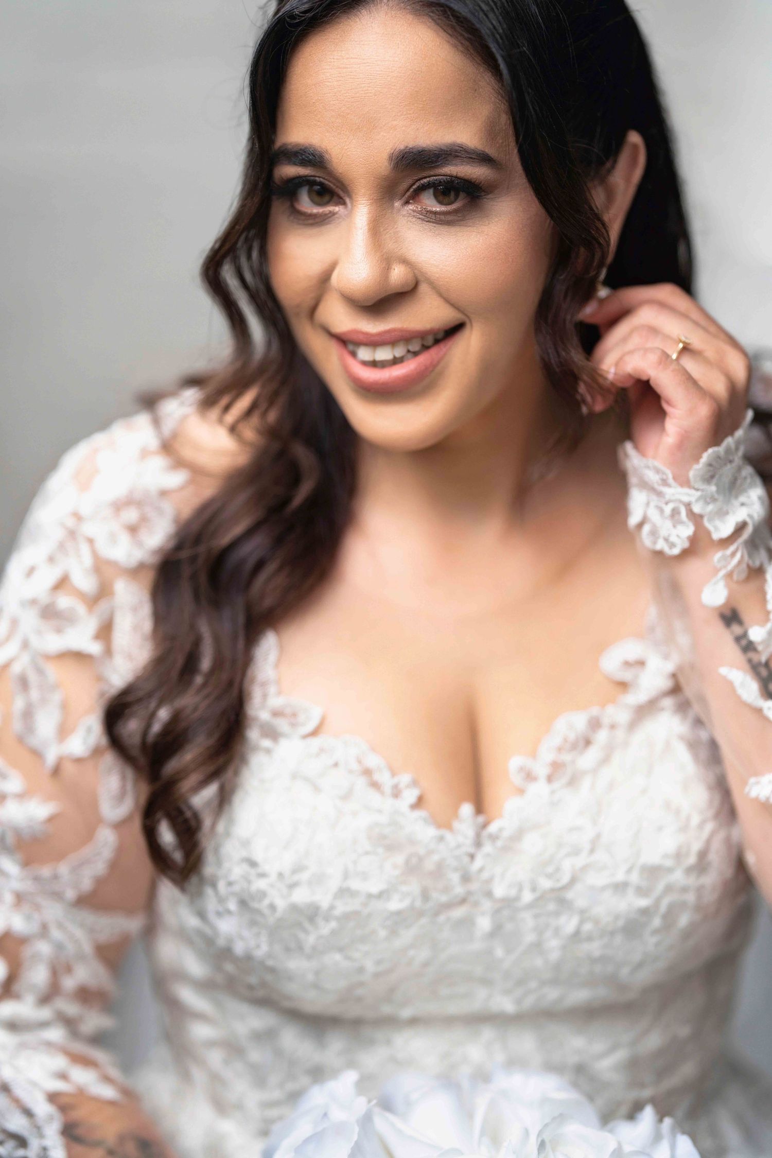 Beautiful bride in lace wedding gown smiles while adjusting earring, close-up portrait.