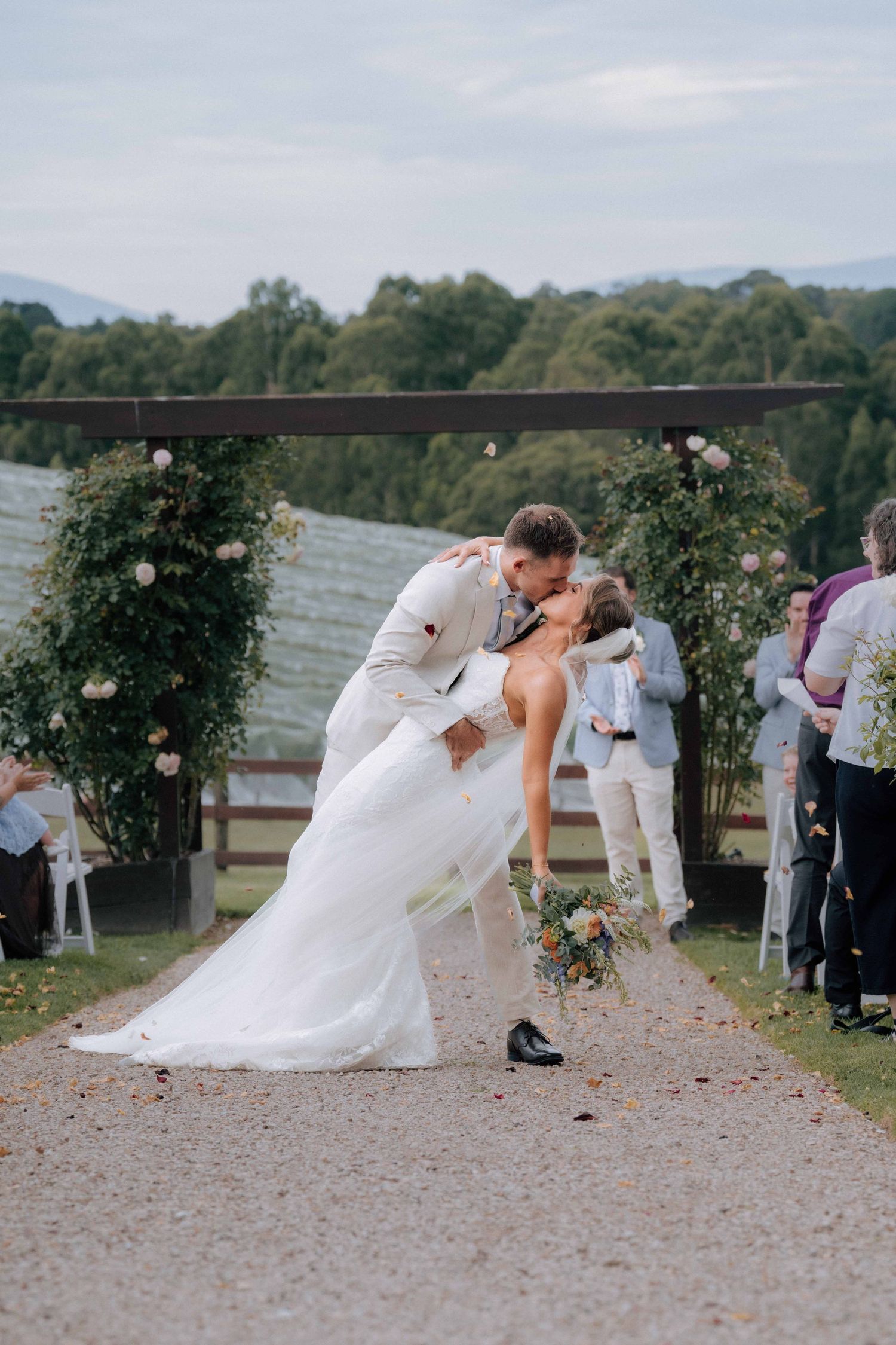 Groom dipping bride for romantic kiss after outdoor wedding ceremony at vineyard venue.