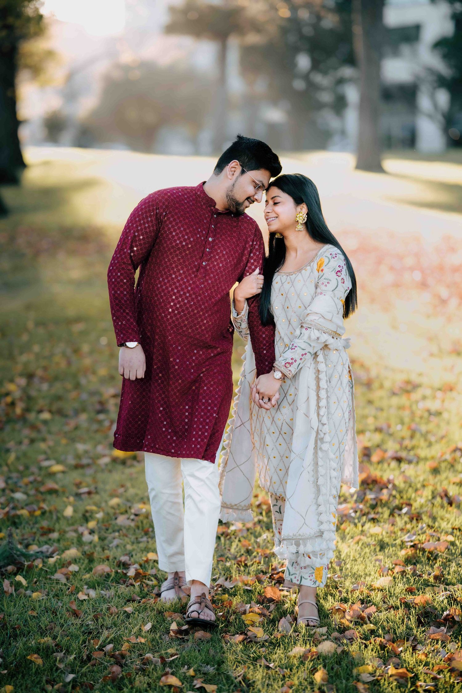 Couple in traditional South Asian attire sharing a romantic moment in an autumn park.