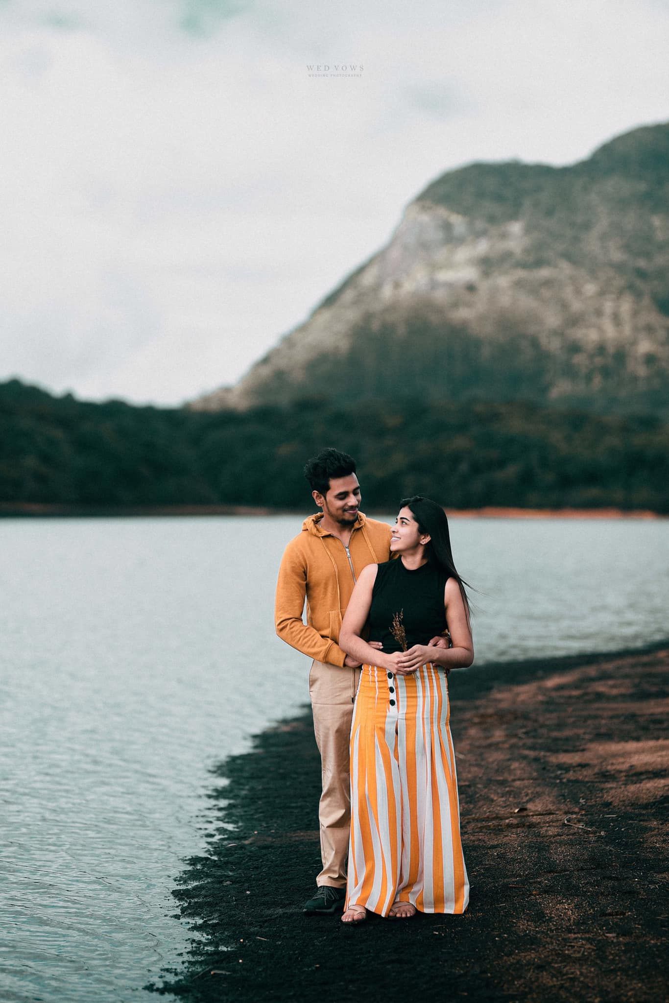 Couple sharing a tender moment by a serene lake with a mountain backdrop.