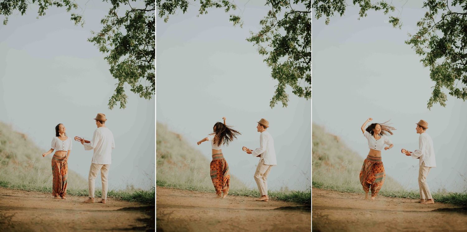 A joyful couple dancing and spinning together on a sunlit dirt path beneath green tree branches.