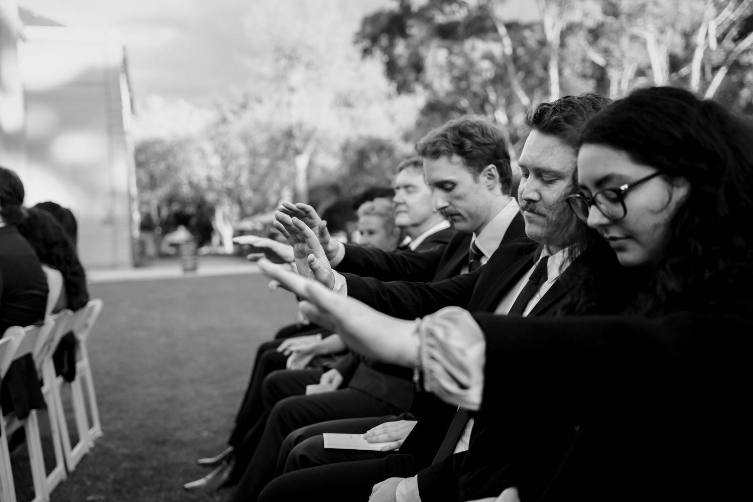 Black and white photo of wedding guests seated in white chairs during outdoor ceremony.