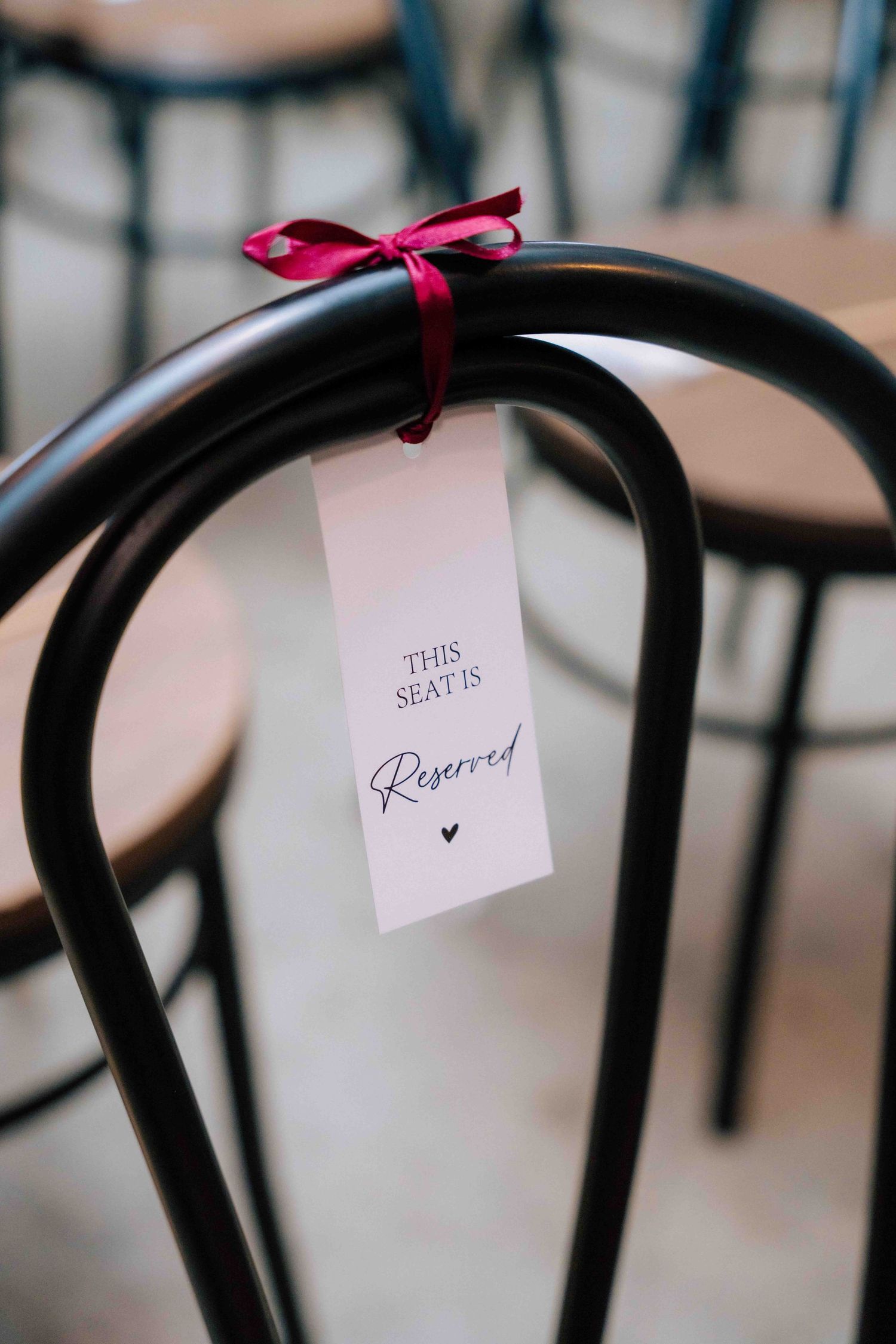 A reserved seat sign tied with a red ribbon on a black chair at a wedding venue.