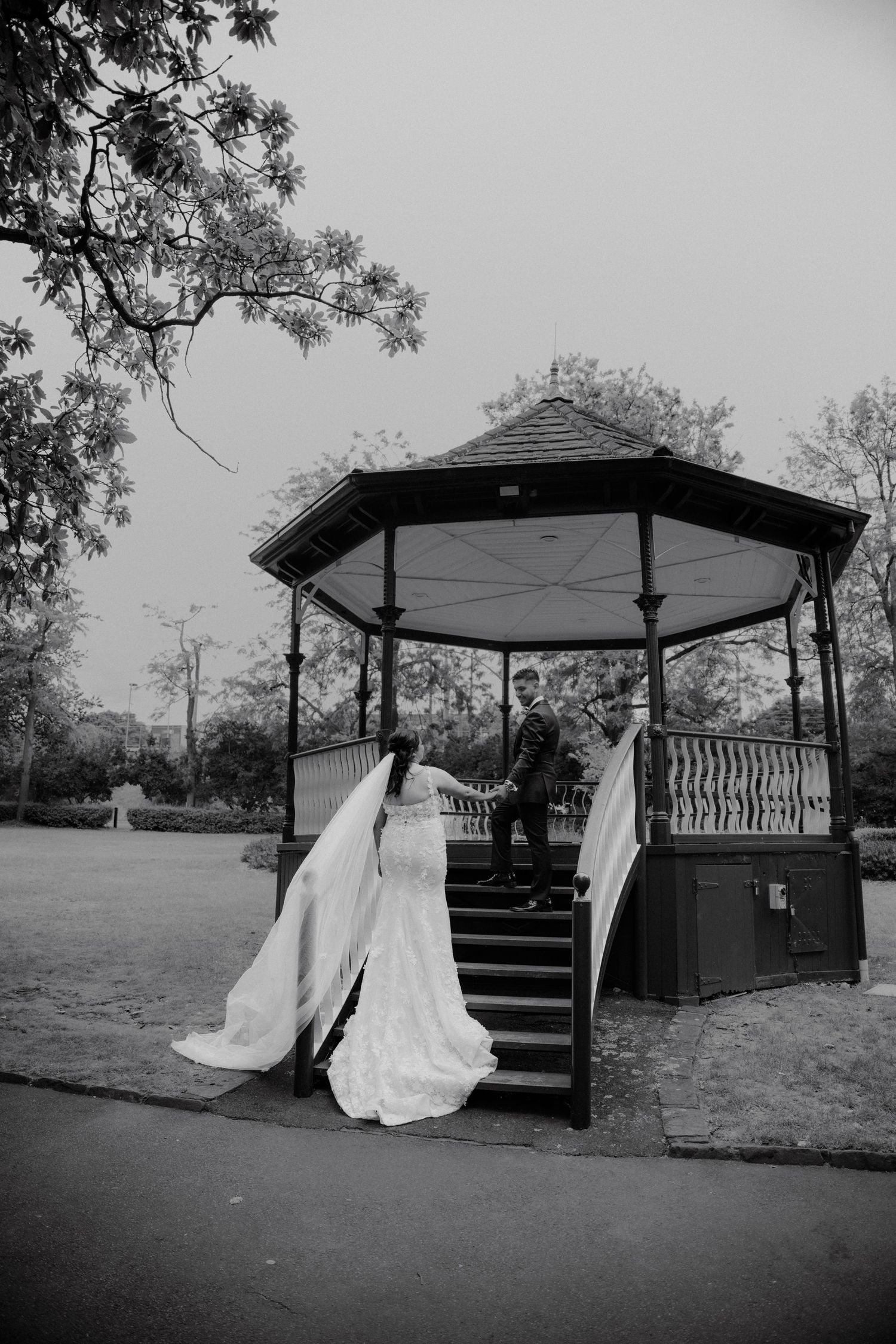 Black and white photo of bride in flowing gown ascending gazebo steps to meet groom.