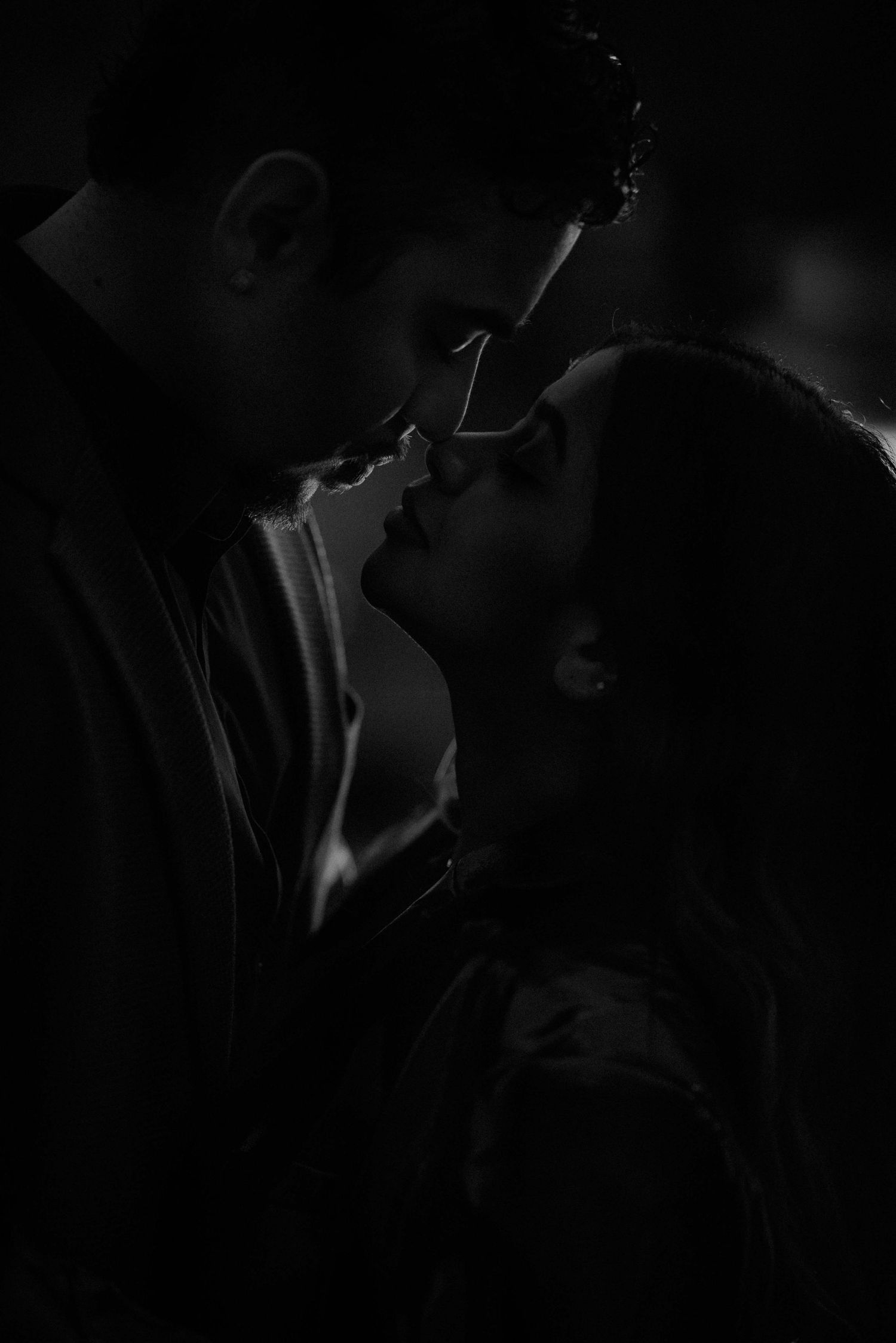 Dramatic black and white close-up of a couple leaning in for a kiss in the dark.
