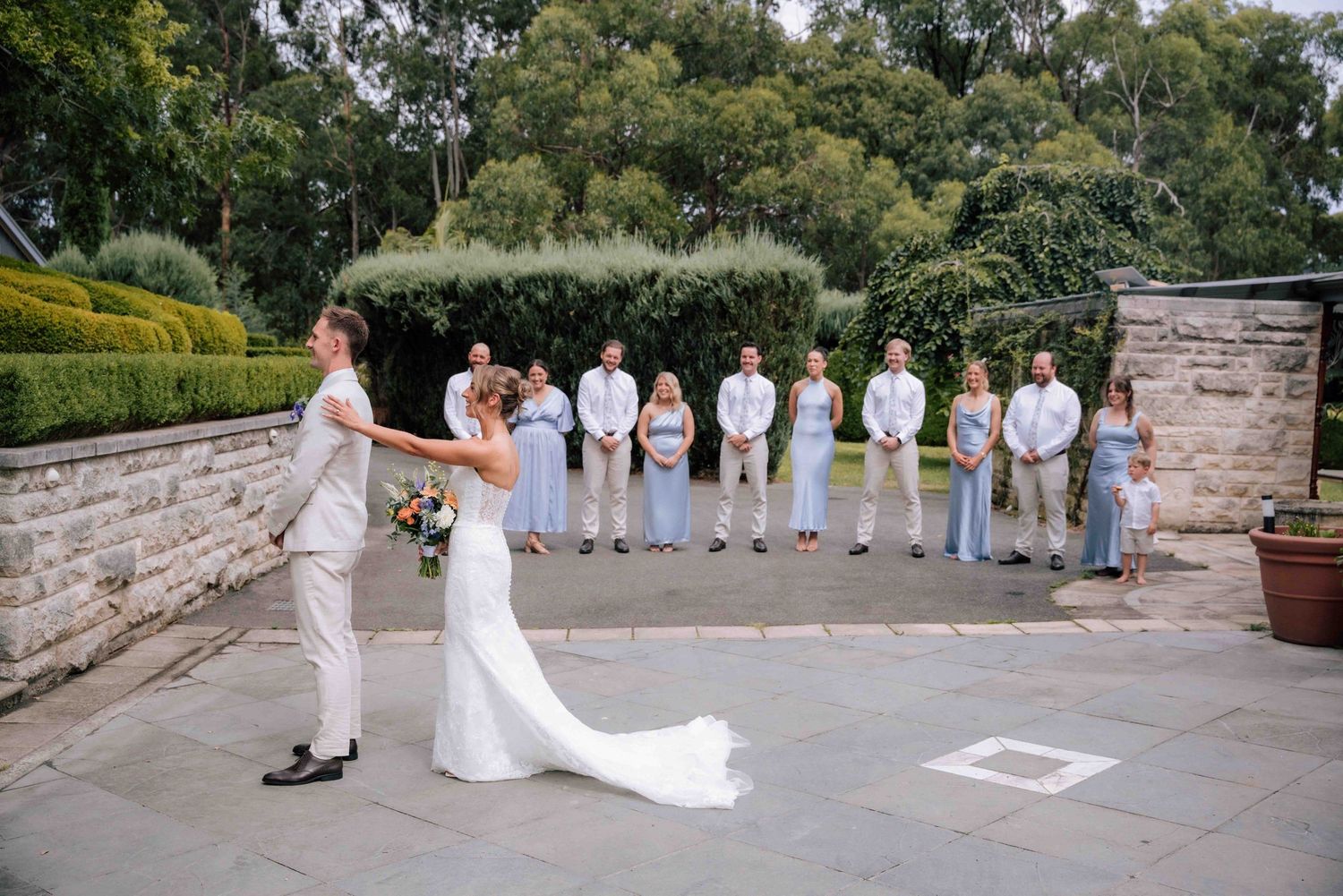 Groom reacts with joy seeing bride in white dress during first look on elegant stone courtyard.