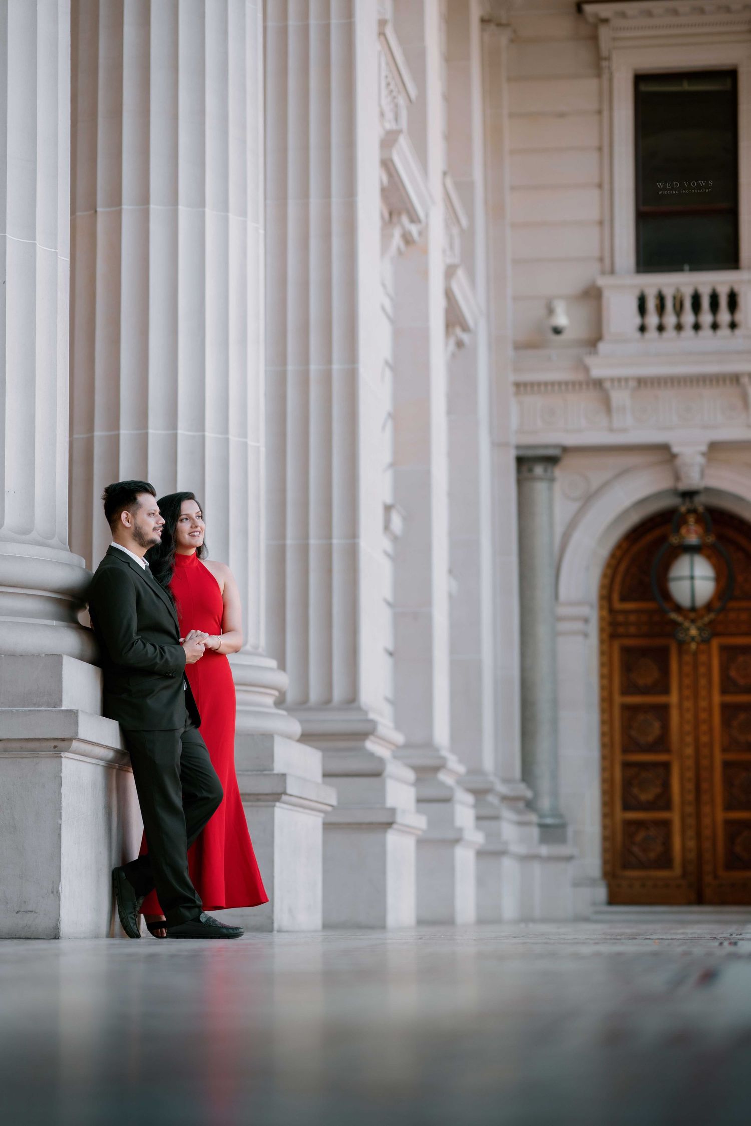 Couple in red dress and dark suit standing by grand white columns of a neoclassical building.