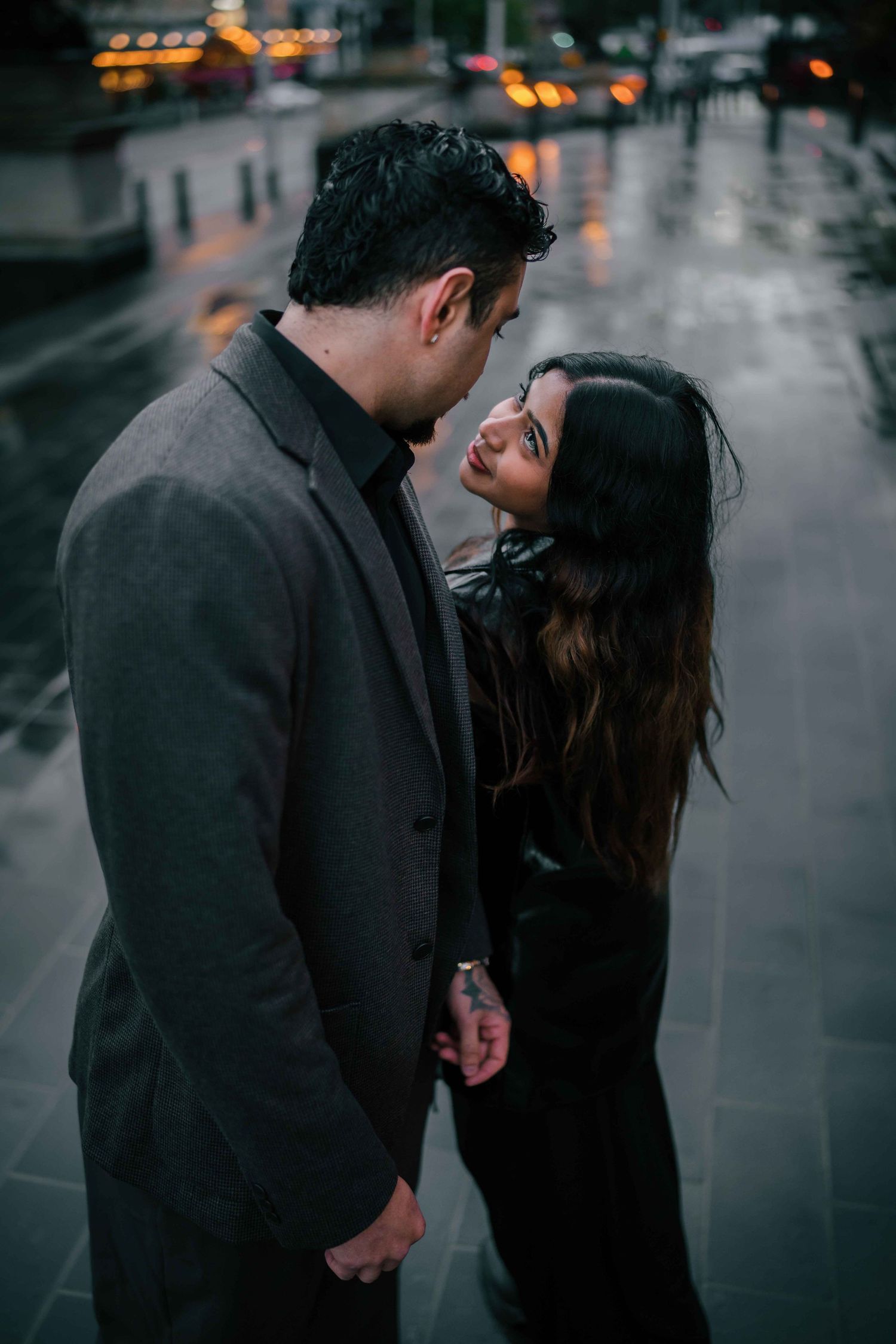 Couple standing close together holding hands on a wet city street in the evening rain.