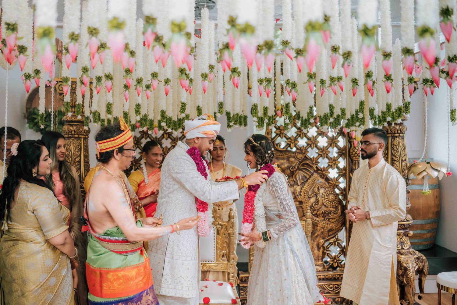 Hindu wedding ceremony with bride and groom exchanging garlands surrounded by family at mandap.