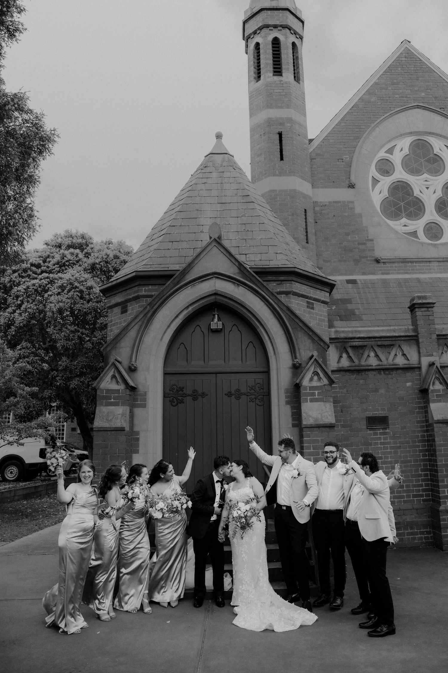 Wedding party celebrating outside historic brick church in black and white photo.