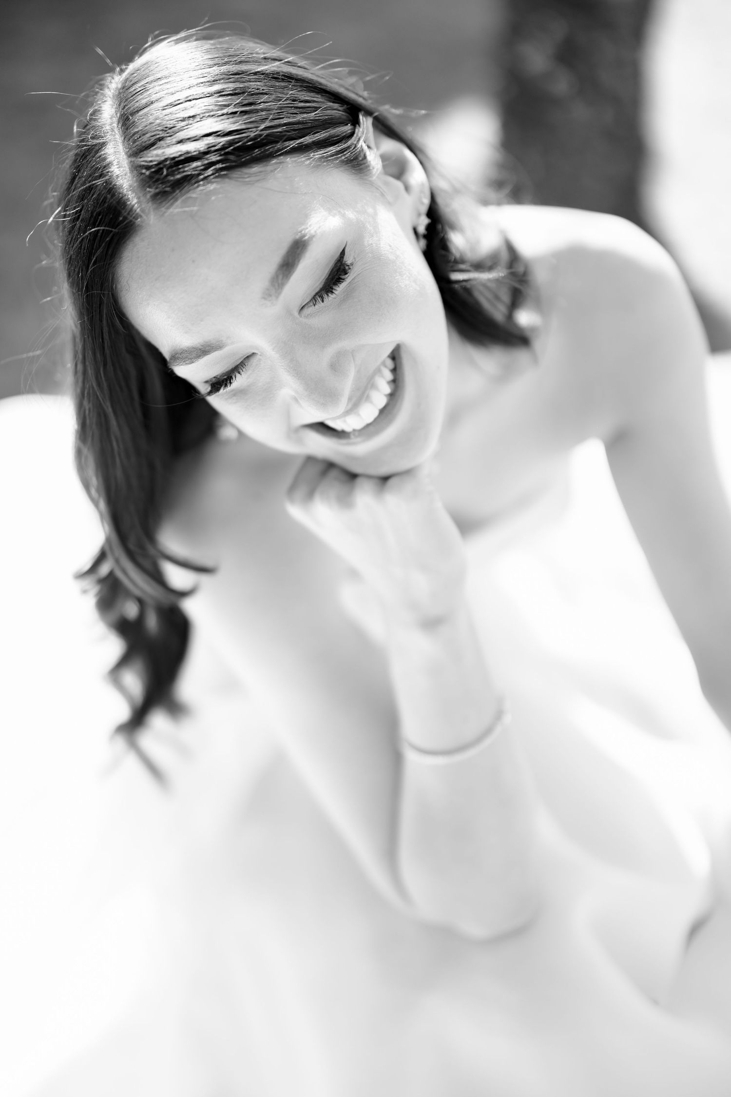 Black and white photo of a laughing bride in a white dress, radiating joy on her wedding day.
