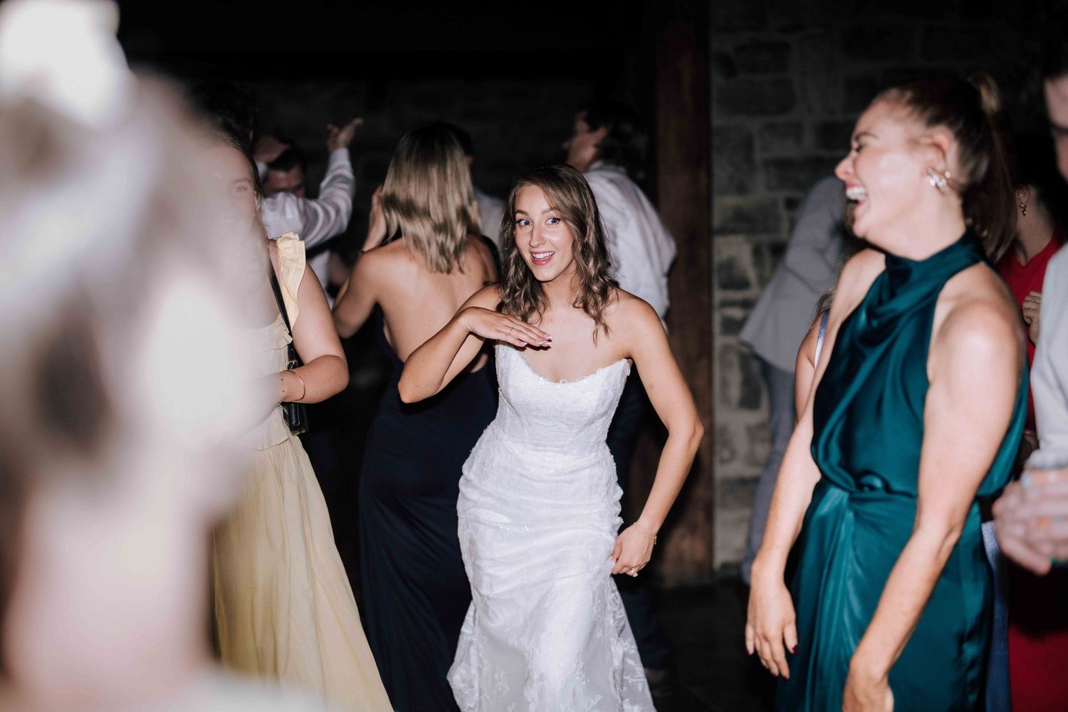 Bride in white gown dances joyfully with guests at wedding reception.