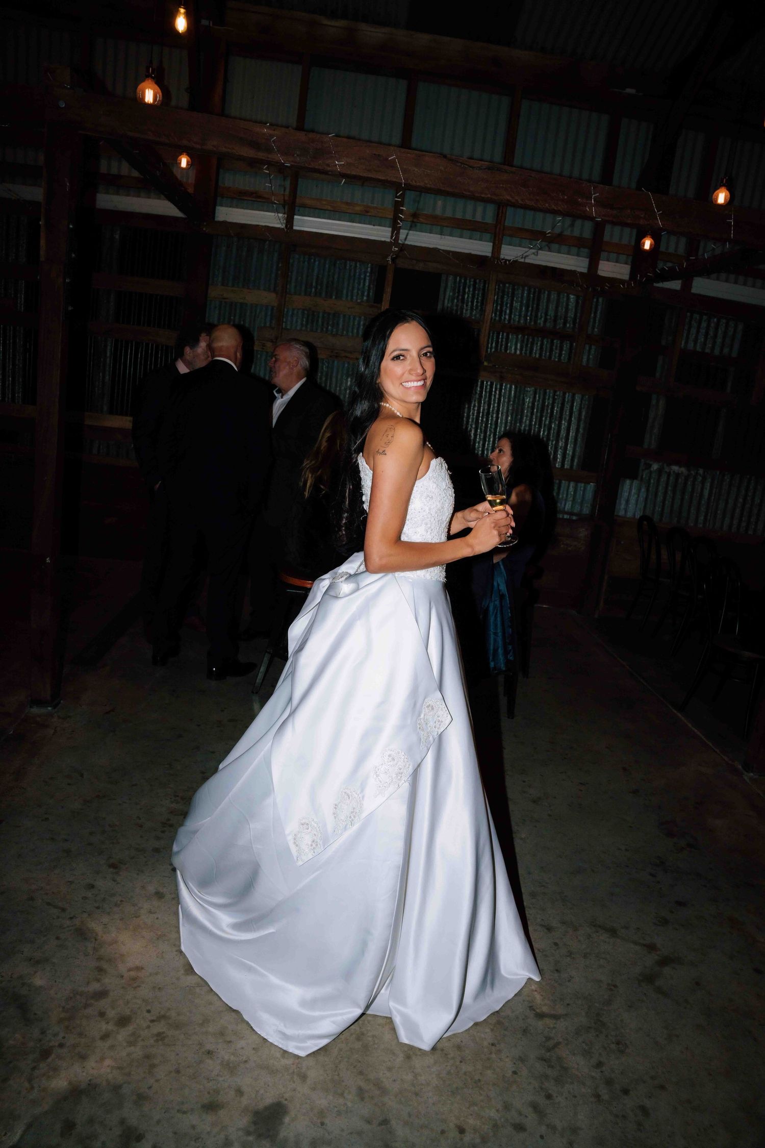 Bride in an elegant white satin ballgown smiling at a rustic barn wedding reception venue.