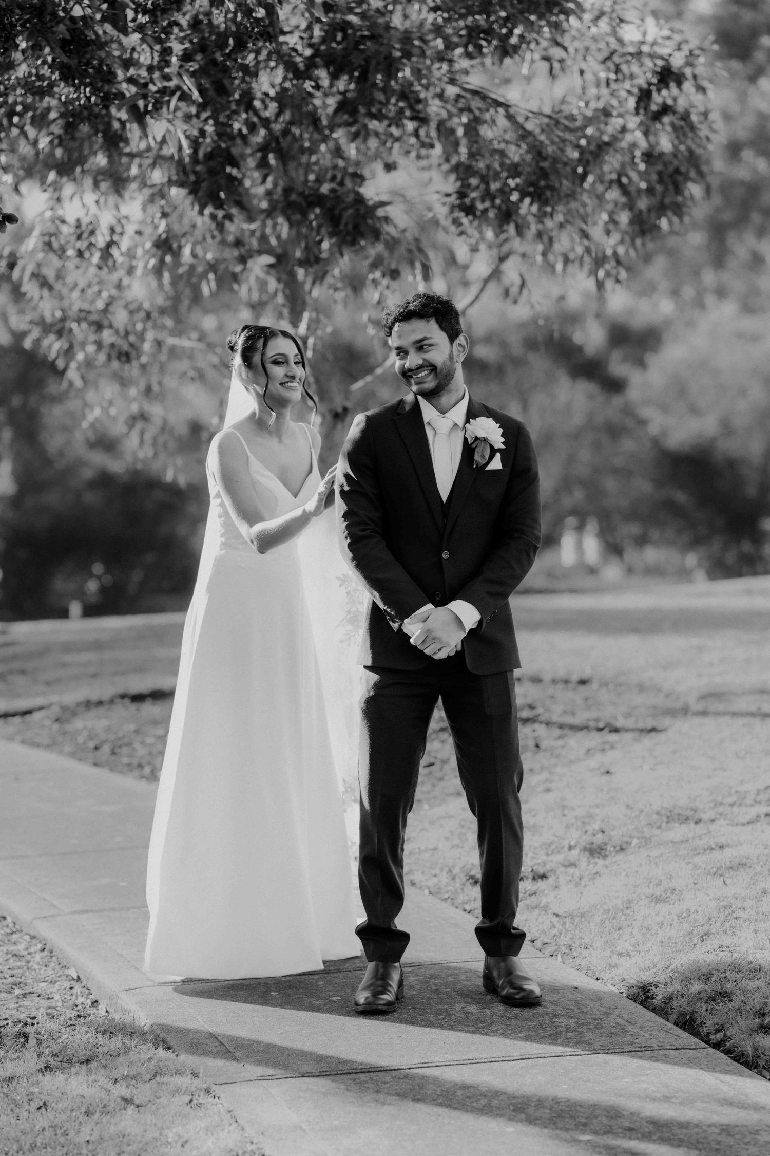 Black and white photo of smiling bride and groom standing together on garden pathway after ceremony.