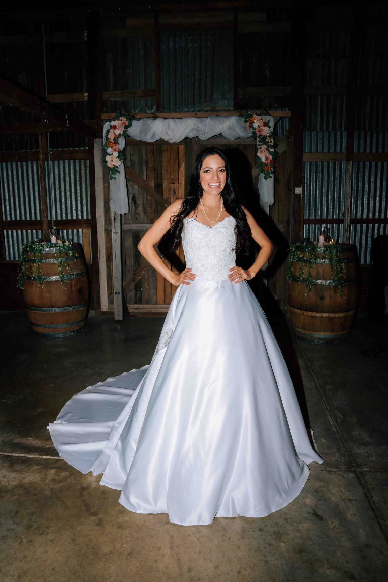 Elegant bride in a satin ball gown with lace bodice poses confidently inside a rustic barn wedding venue.
